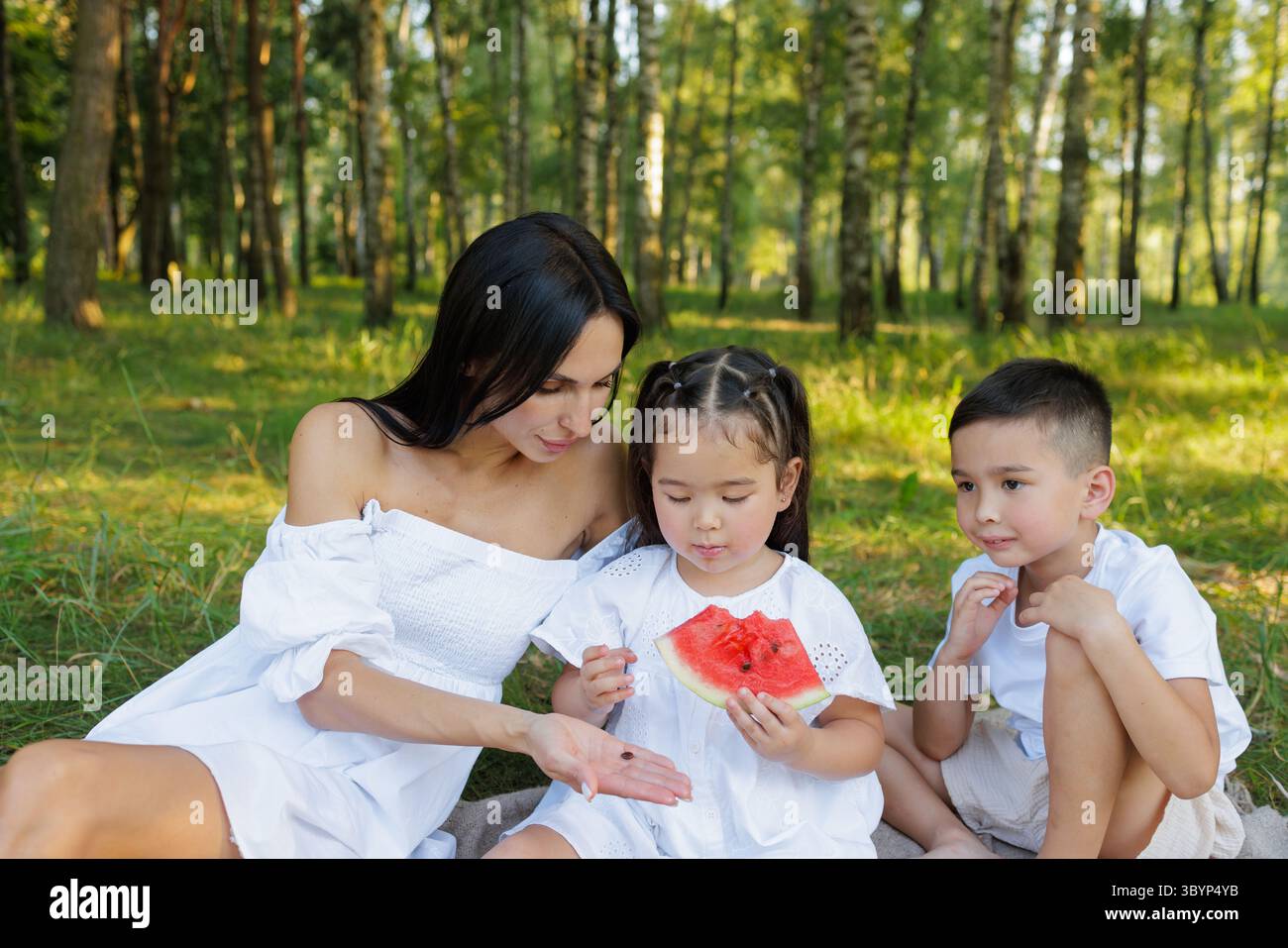 Glückliche Mutter und Kinder essen Wassermelone beim Picknick im Sommerwald, Familie verbindet Pflege und Freude in der Natur Stockfoto