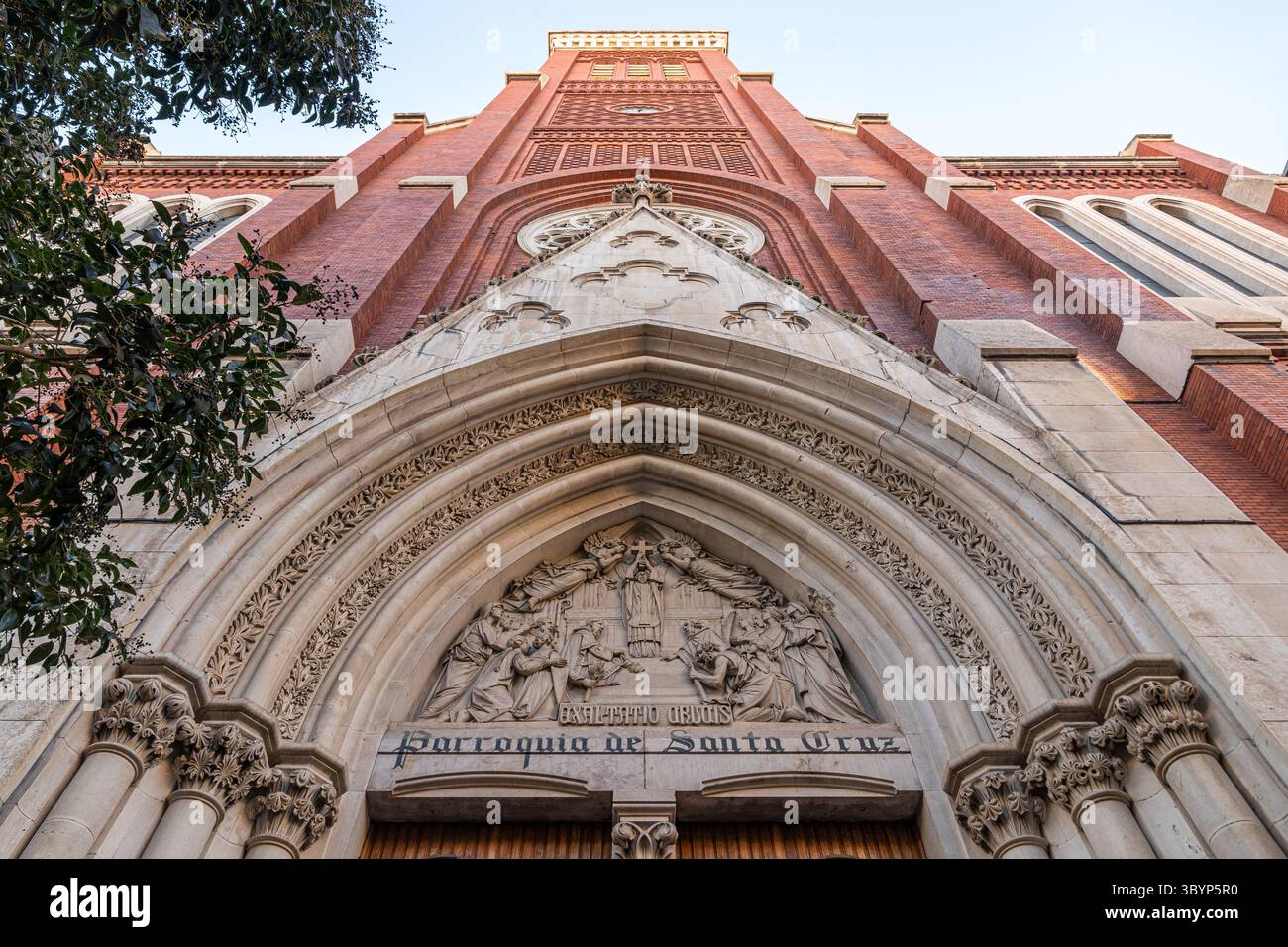 Madrid, Spanien. Kirche Santa Cruz in Atocha 6 aus neogotischen Backsteinen und weißem Stein, mit spitzem Bogeneingang, Rosenfenster und einem hohen Turm, der sich darüber erhebt Stockfoto