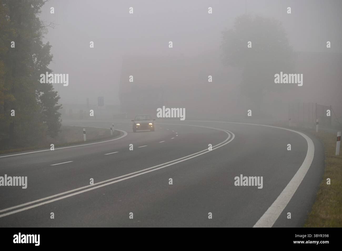 Autos im Nebel. Schlechtes Winterwetter und gefährlicher Autoverkehr auf der Straße. Leichte Fahrzeuge im Nebel Stockfoto