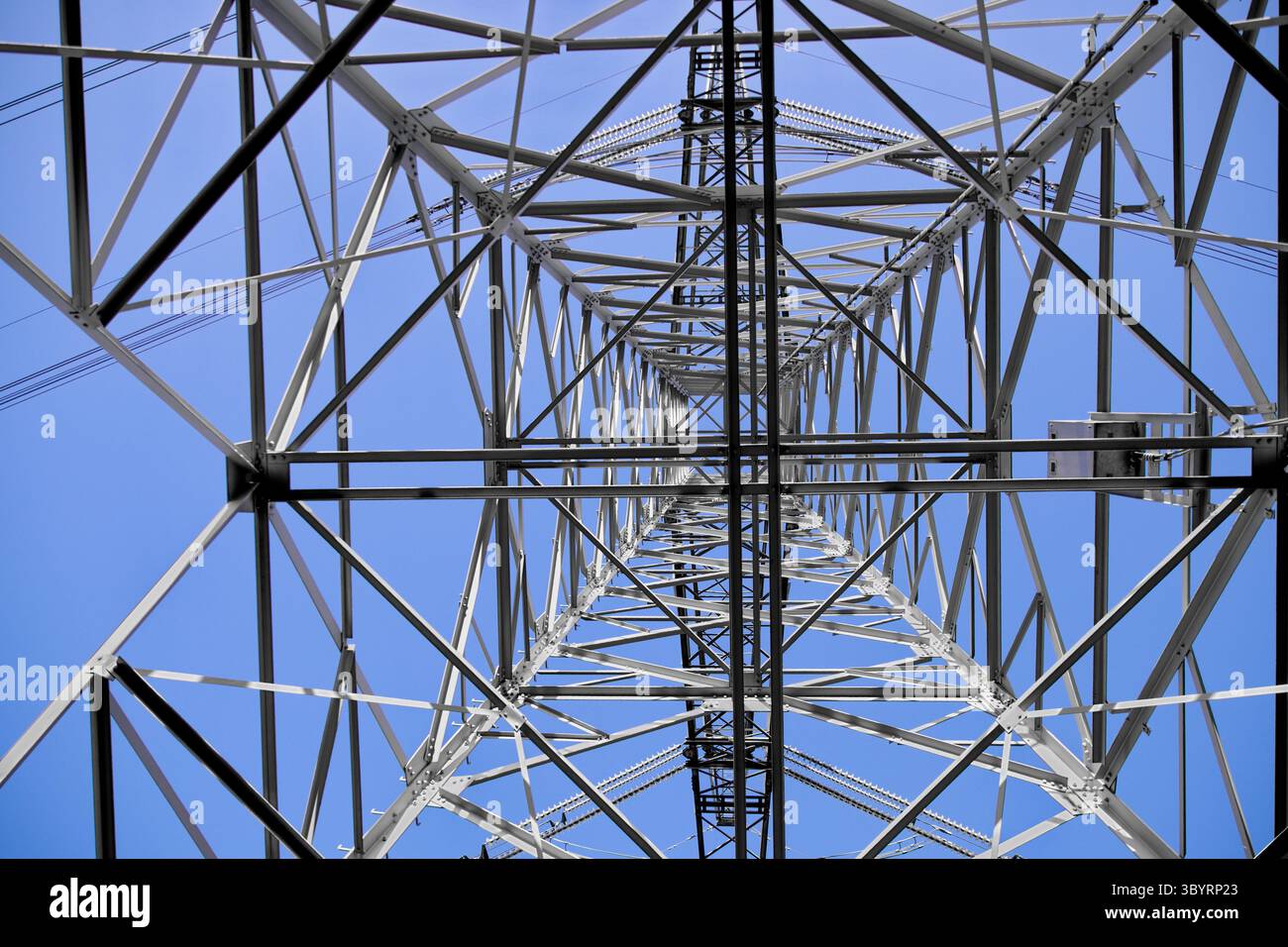Blick nach oben durch das Stahlgitter eines Hochspannungs-Sendeturms und enthüllt komplexe, kühne Industriegeometrie vor einem klaren blauen Himmel. Stockfoto Blick nach oben durch das Stahlgitter eines Hochspannungs-Sendeturms und enthüllt komplexe, kühne Industriegeometrie vor einem klaren blauen Himmel. Stockfoto
