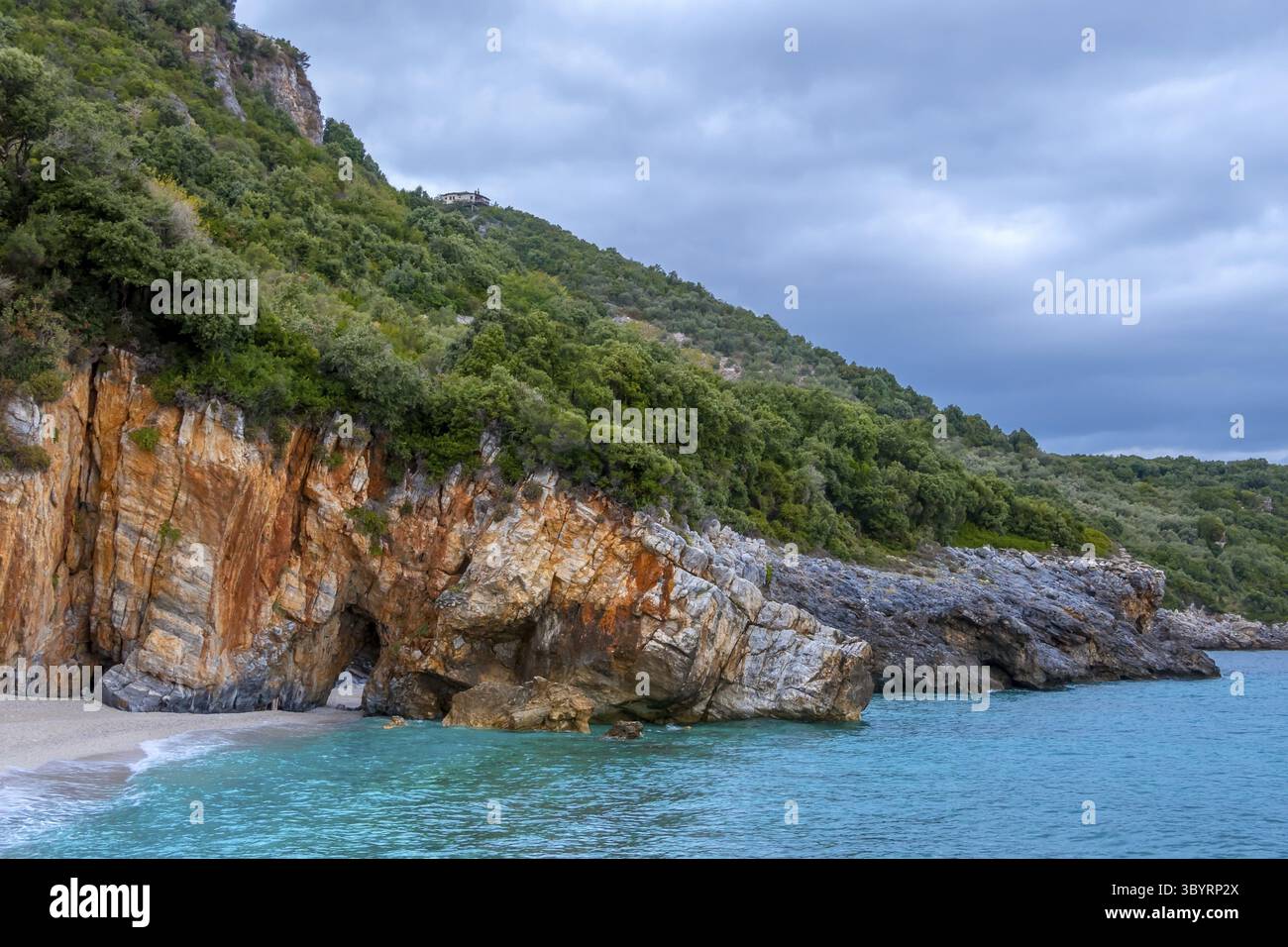 Felsigen Wald Ufer des Meeres bei bewölktem Himmel. Villa am Hang. Gibt es einen natürlichen Steinbogen am Strand Stockfoto