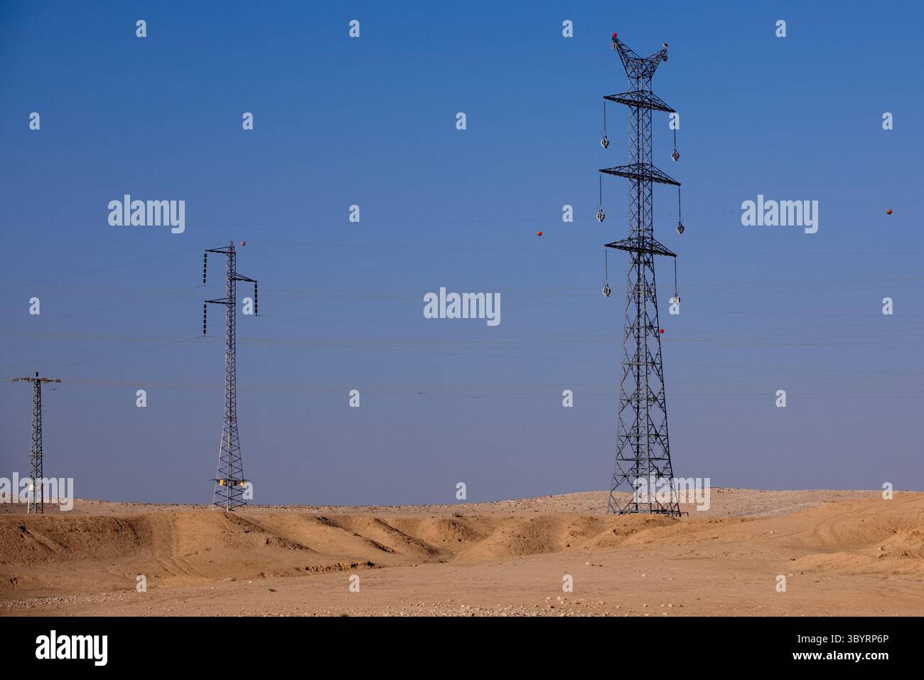 Sonnendurchflutete Hochspannungstürme unterstreichen einen weiten Wüstenhorizont unter einem strahlend blauen Himmel und zeigen industrielle Kunstfertigkeit und geometrische Eleganz in rauer aussicht. Stockfoto Sonnendurchflutete Hochspannungstürme unterstreichen einen weiten Wüstenhorizont unter einem strahlend blauen Himmel und zeigen industrielle Kunstfertigkeit und geometrische Eleganz in rauer aussicht. Stockfoto