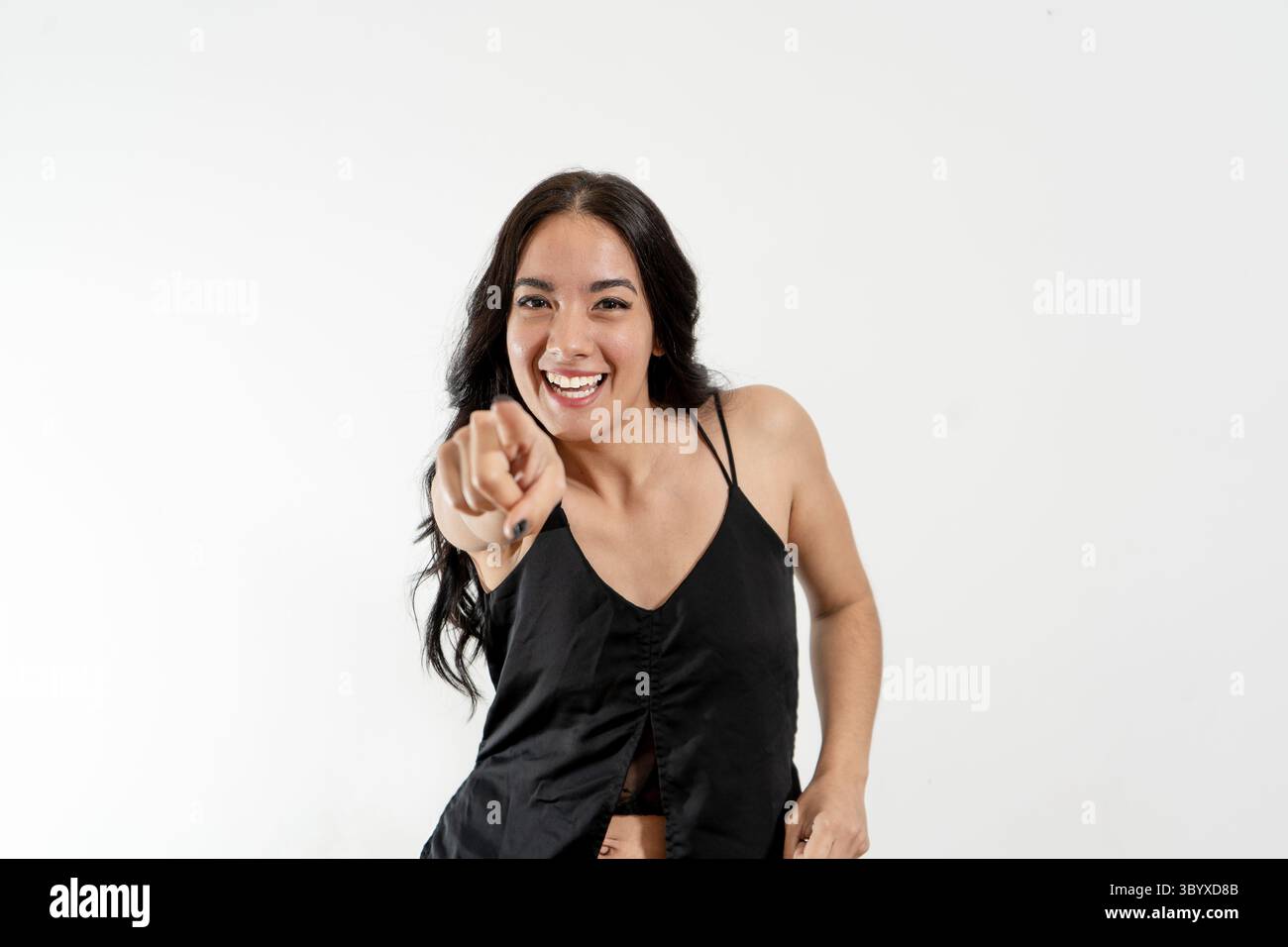 Glückliche junge Frau mit langen dunklen Haaren, die nach vorne zeigen und lachen, isoliert auf weißem Hintergrund Stockfoto