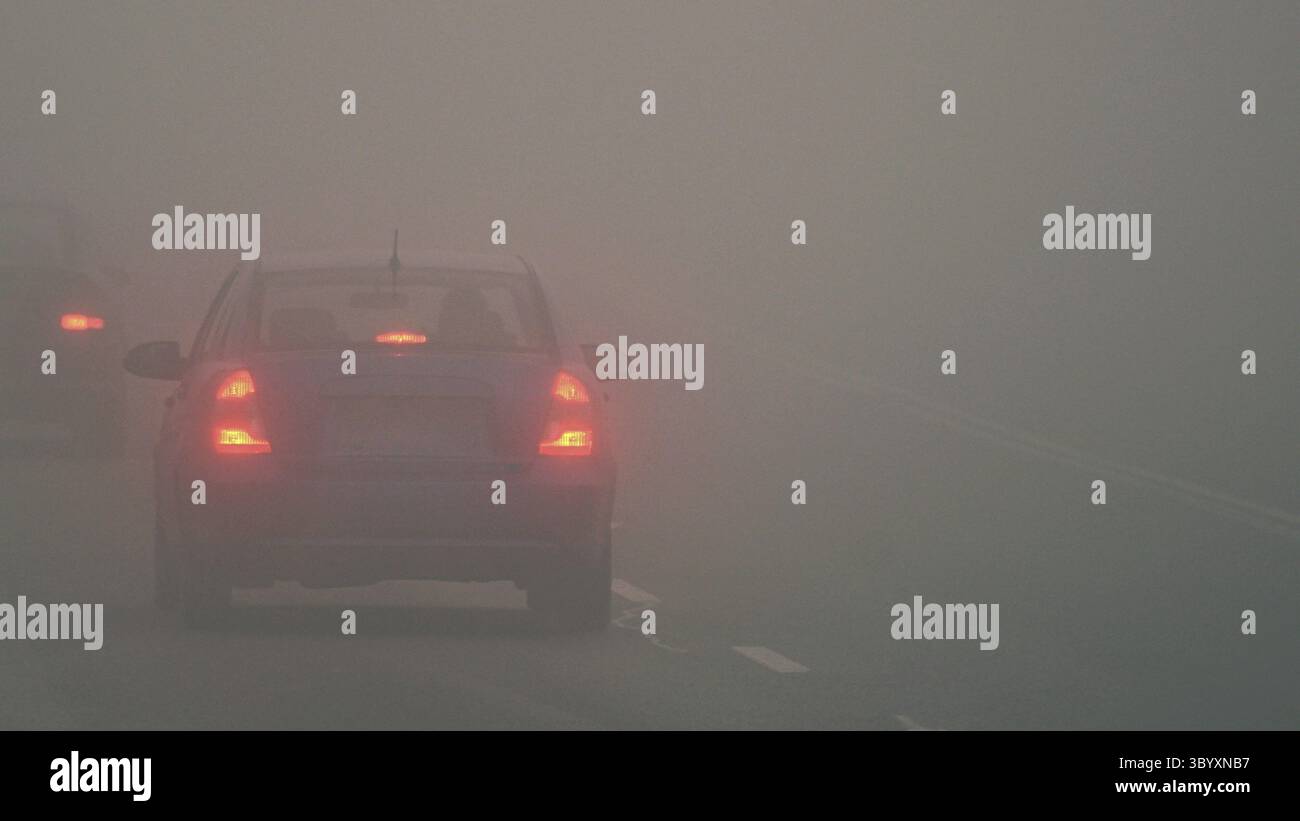 Autos im Nebel. Schlechtes Winterwetter und gefährlicher Autoverkehr auf der Straße. Leichte Fahrzeuge im Nebel Stockfoto
