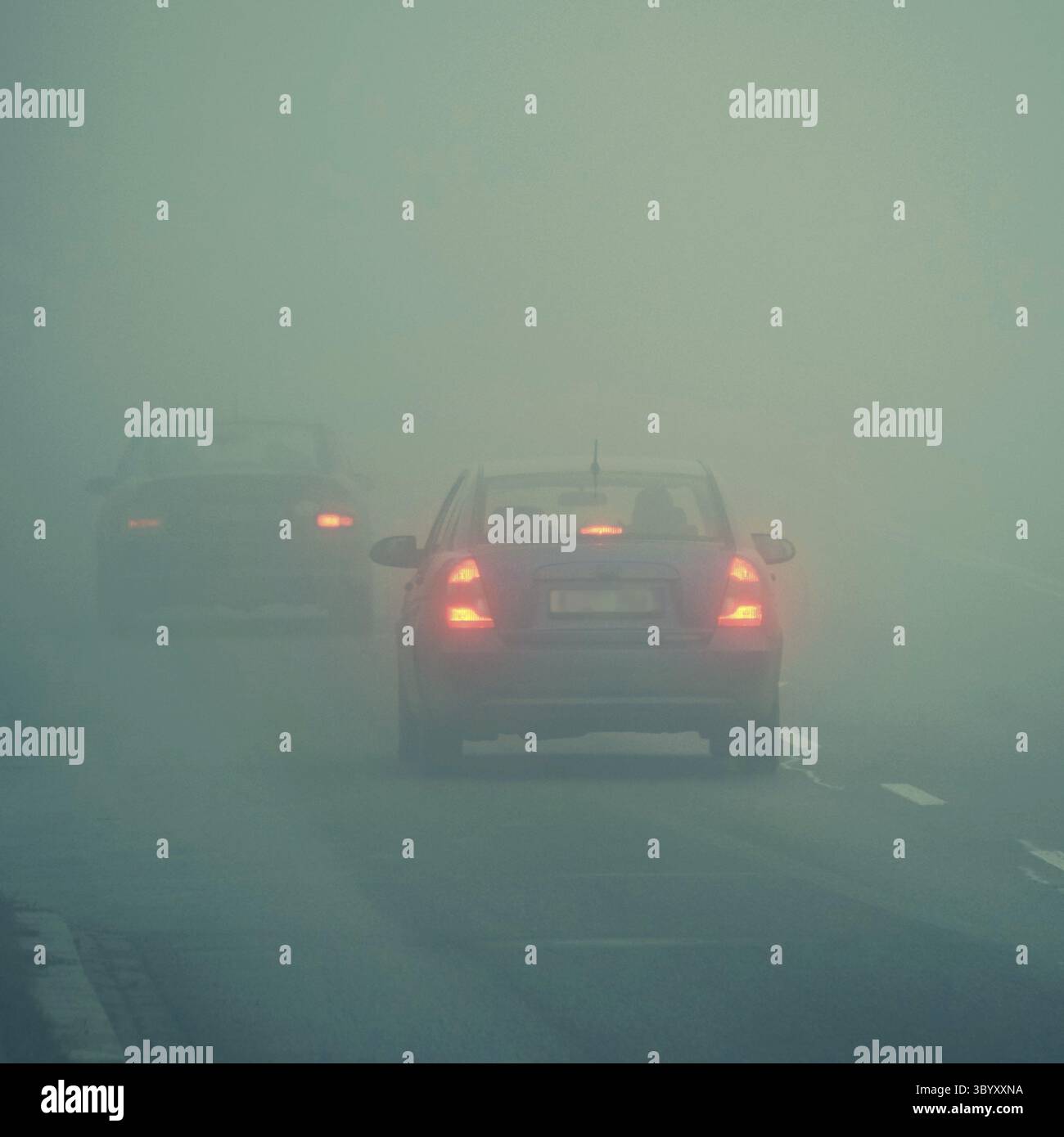 Autos im Nebel. Schlechtes Winterwetter und gefährlicher Autoverkehr auf der Straße. Leichte Fahrzeuge im Nebel Stockfoto