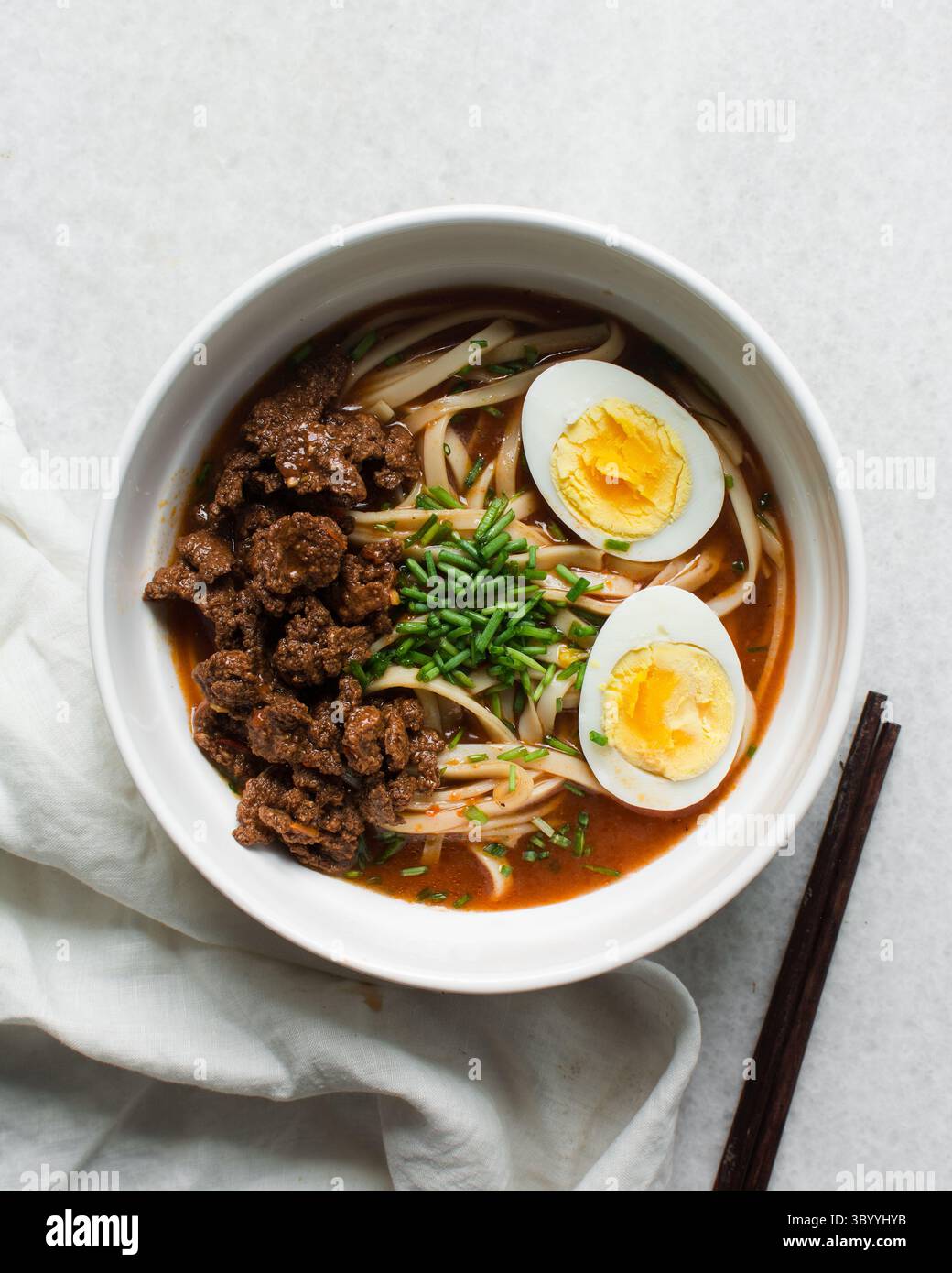 Blick von oben auf scharfe Nudelsuppe mit Eiern und Rindfleischstücken in einer weißen Schüssel, Blick von oben auf Nudeln Eier in einer scharfen Brühe mit Zwiebeln Stockfoto