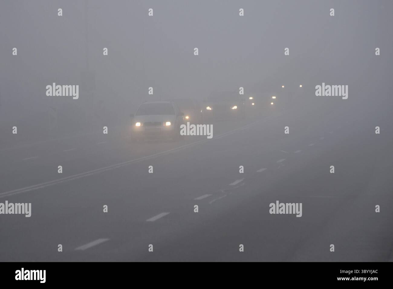 Autos im Nebel. Schlechtes Winterwetter und gefährlicher Autoverkehr auf der Straße. Leichte Fahrzeuge im Nebel Stockfoto