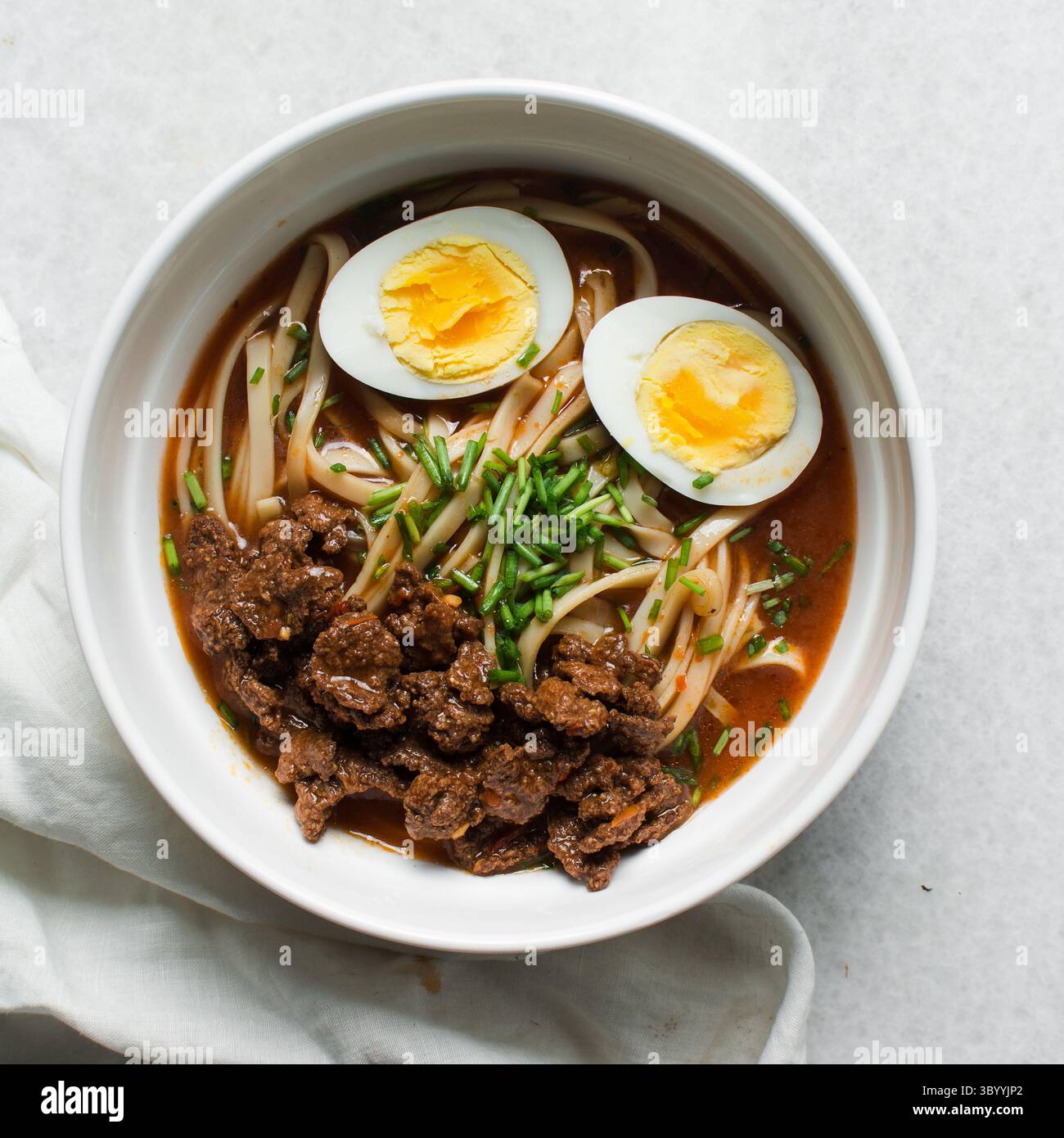 Blick von oben auf scharfe Nudelsuppe mit Eiern und Rindfleischstücken in einer weißen Schüssel, Blick von oben auf Nudeln Eier in einer scharfen Brühe mit Zwiebeln Stockfoto
