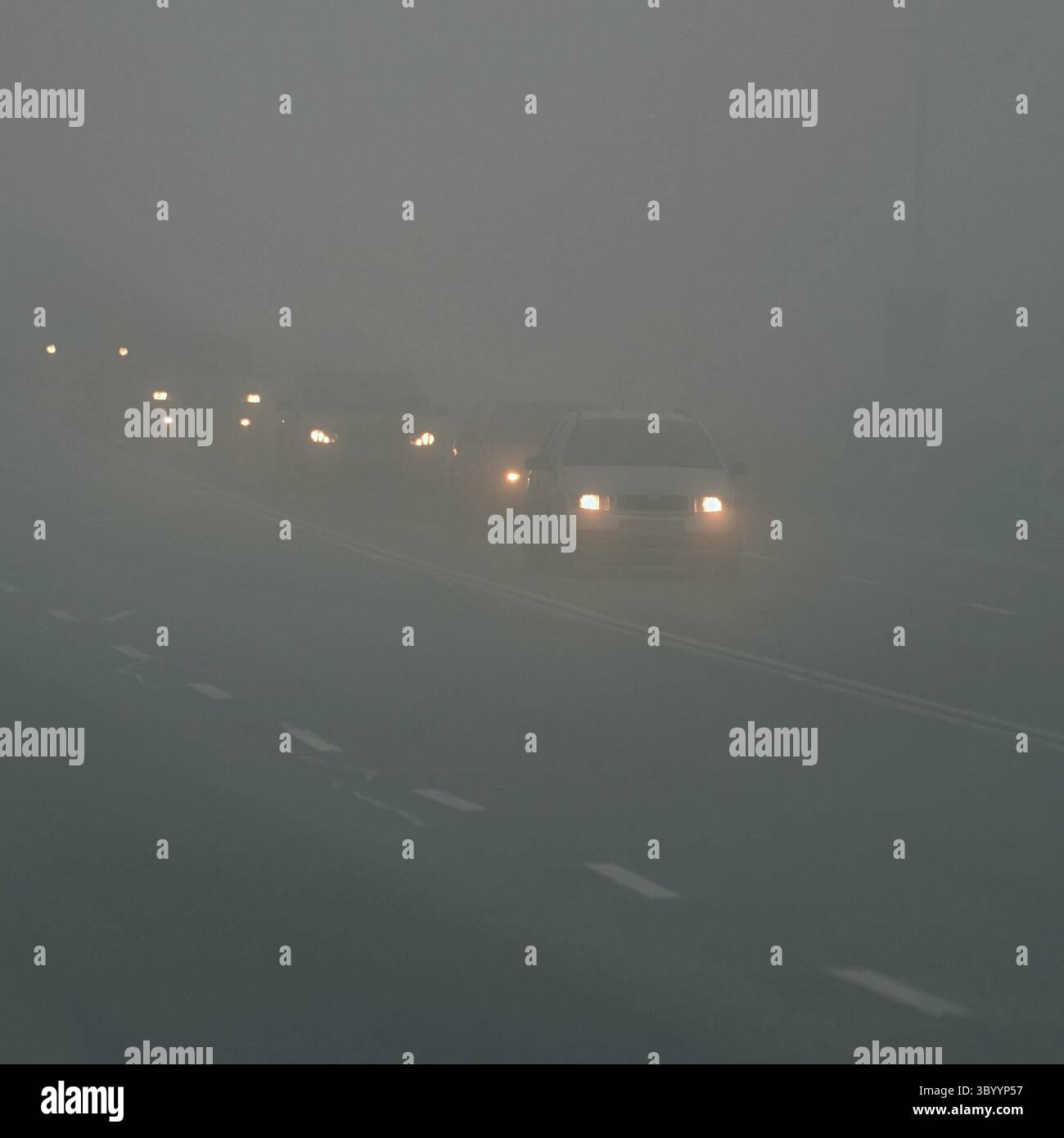 Autos im Nebel. Schlechtes Winterwetter und gefährlicher Autoverkehr auf der Straße. Leichte Fahrzeuge im Nebel Stockfoto
