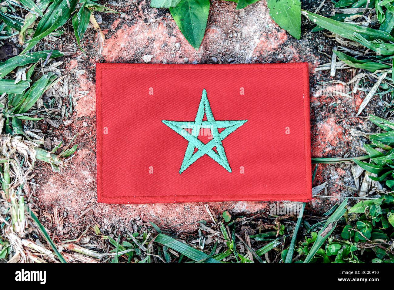 Marokkanische Flagge im Öko-Stil aus Faden, zentriert auf einem alten Felsen mit grünem Rand. Ideal für den Tag der Erde, Klimaprobleme und umweltfreundliche Reisebilder. Stockfoto