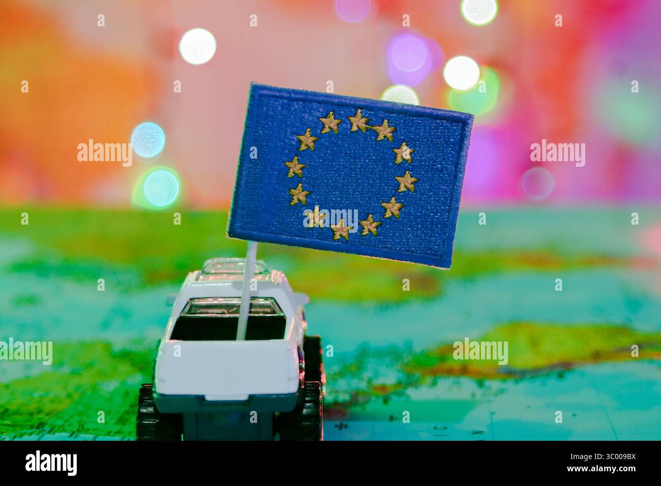 Spielzeug-Pickup mit EU-Flagge auf einem Weltkartenhintergrund in Richtung lebendiger Bokeh-Lichter, symbolisches Bild der globalen Feier und des internationalen Tourismus Stockfoto