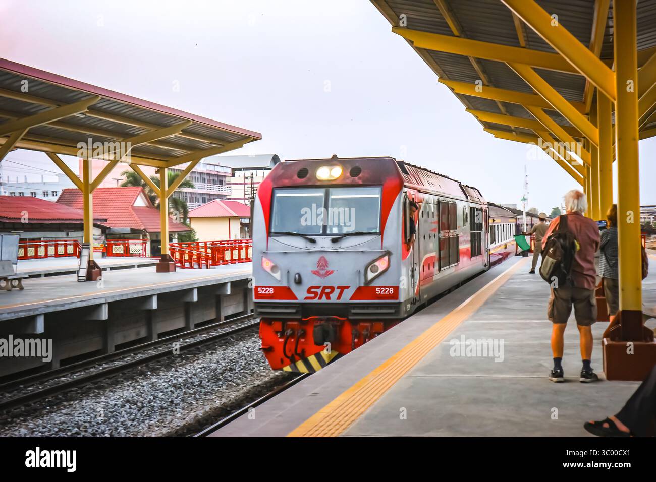 Eine thailändische Lokomotive fährt in einen pulsierenden gelben Bahnhof, während Touristen auf das Einsteigen warten. Ideal für Reisen nach Asien, Kultur und umweltfreundliche Reisen. Stockfoto