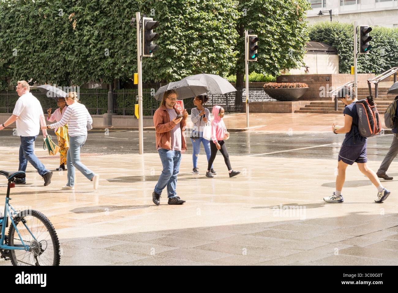 London, Großbritannien - 20. Juli 2025: Wetter in Großbritannien. Besucher der London Canary Wharf, die in Summer Rain and Sunshine gefangen sind – einige mit Regenschirmen, andere ohne Sonnenschein, auf einem Hot Sunday Credit: Glosszoom/Alamy Live News. Stockfoto
