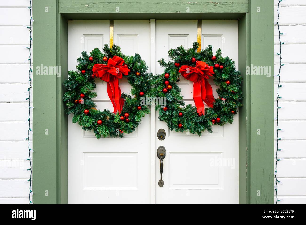 Grüne Weihnachtskränze mit roten Bändern und Kugeln hängen an der Tür Stockfoto