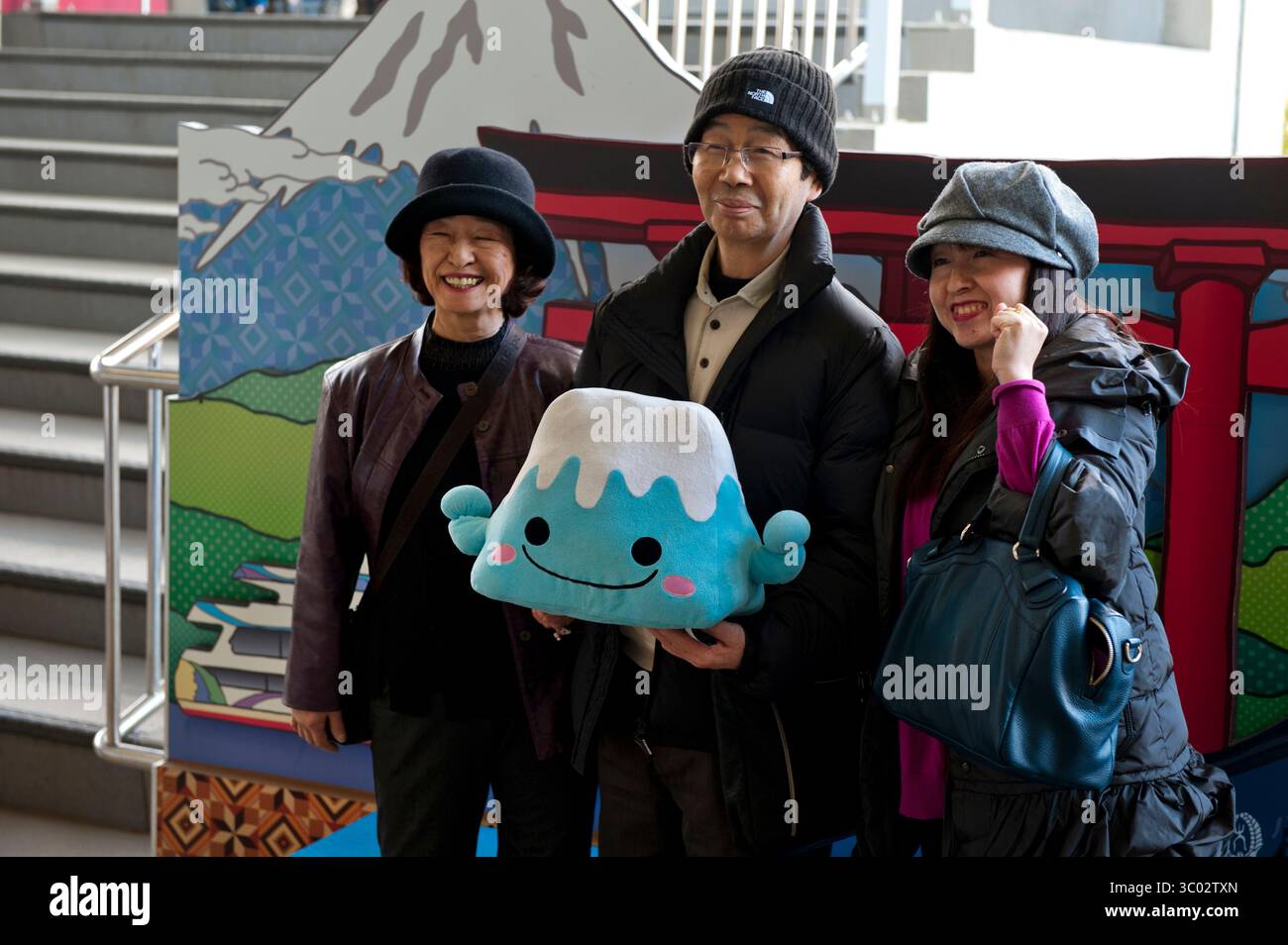 Touristen, die eine Puppe mit dem Charakter des Mount Fuji halten, posieren für ein Erinnerungsfoto in der Seilbahnstation des Mount Komagatake in Hakone-en, Japan. Stockfoto