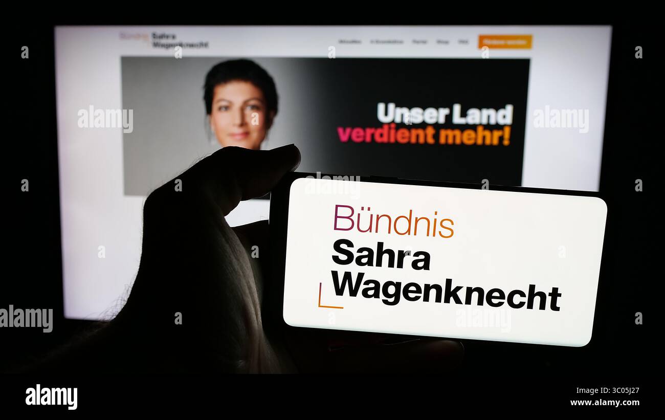 In dieser Fotoabbildung hält eine Person ein Mobiltelefon mit dem Logo der deutschen Partei Bündnis Sahra Wagenknecht (BSW) auf dem Bildschirm vor der Webseite. Stockfoto