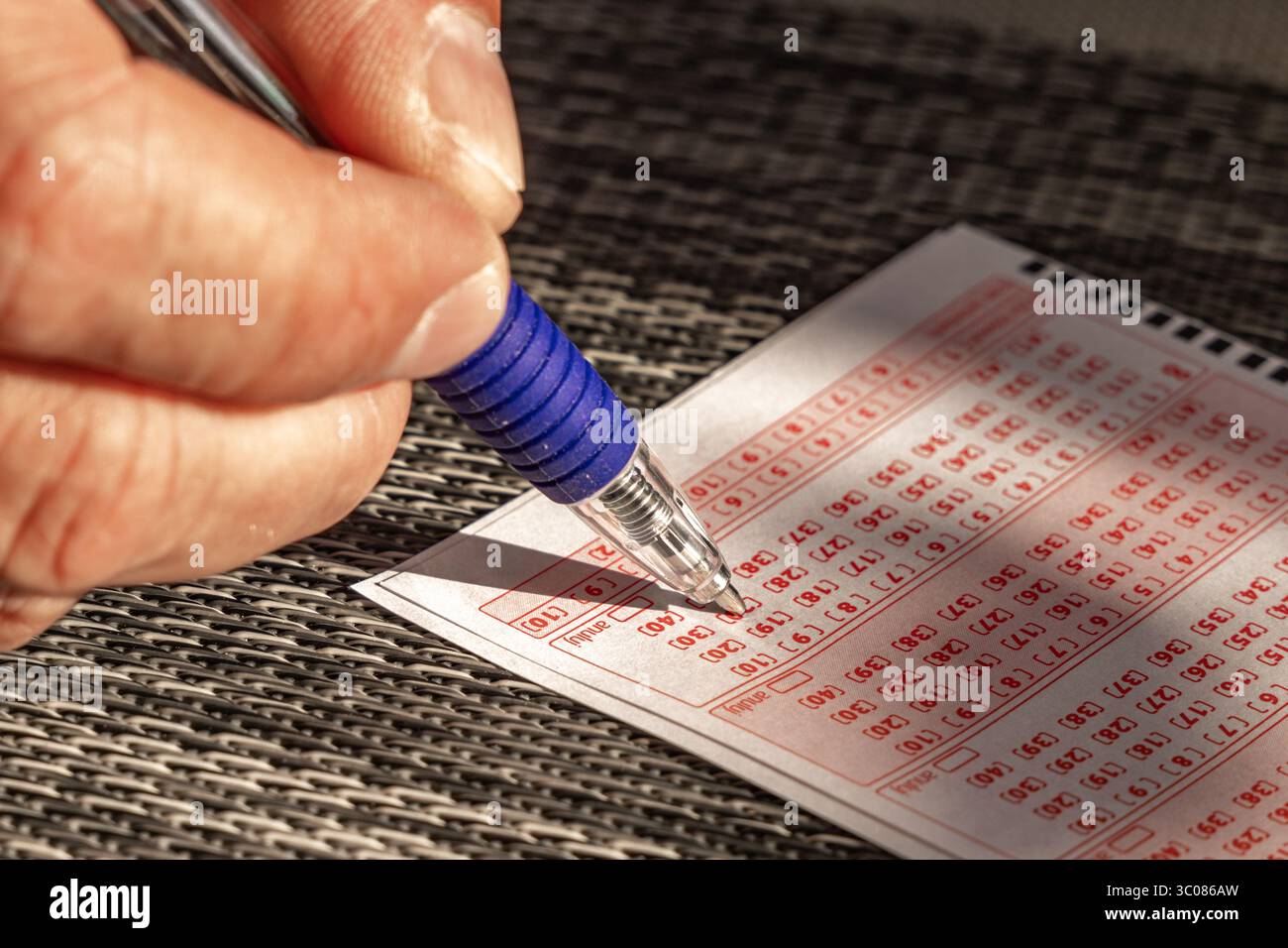Das Ausstreichen von Glückszahlen in einer großen Geldverlosung, ein Lottoticket, das Markieren von Zahlen mit einem Stift auf einem Spielschein Stockfoto