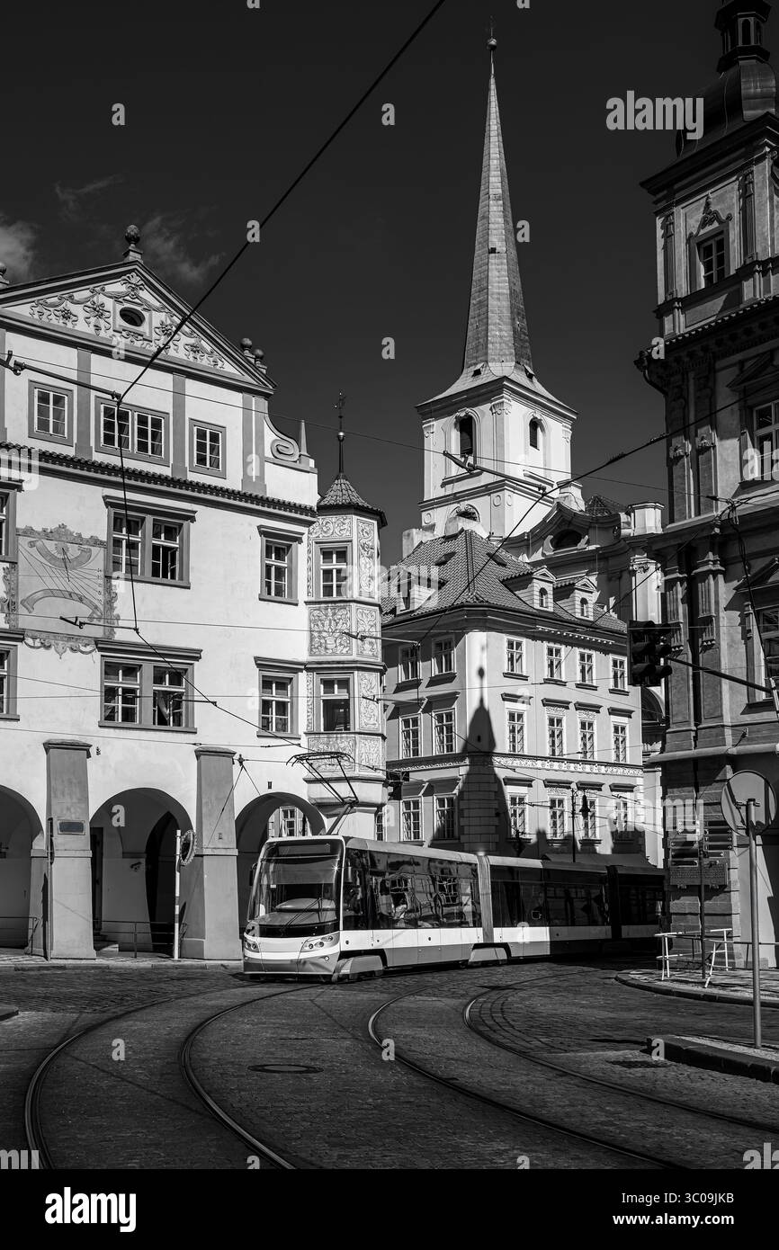 Eine Schwarzweißaufnahme einer modernen Straßenbahn auf der Kopfsteinpflasterstraße, umgeben von historischen Gebäuden in der Prager Altstadt, Tschechien. Stockfoto