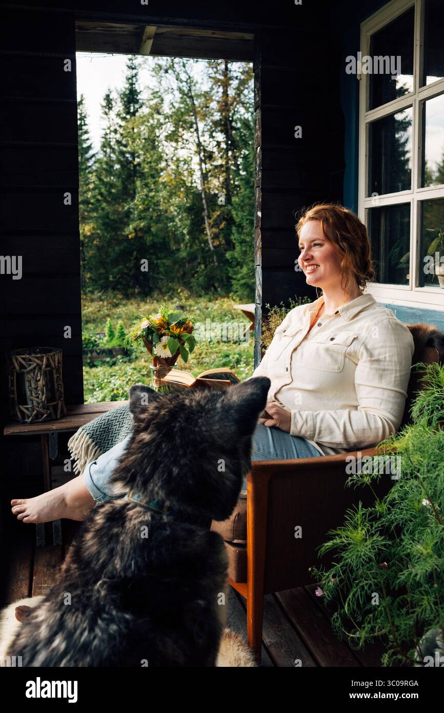Frau, die sich mit dem alaskischen Malamute-Hund auf der Veranda der Hütte in Swede erholt Stockfoto