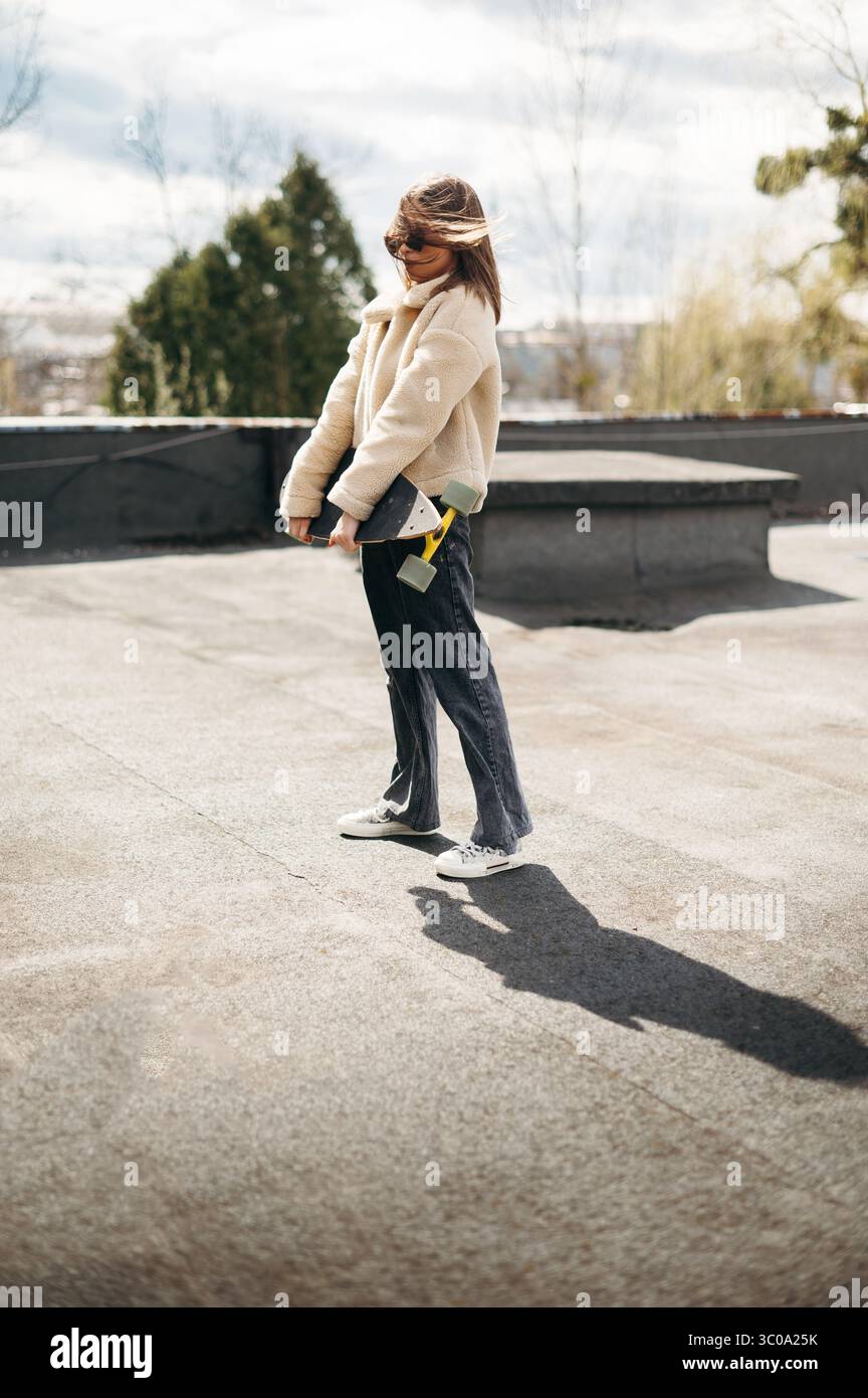 Stilvolle Frau, die Skateboard hält, während sie auf dem Dach steht Stockfoto