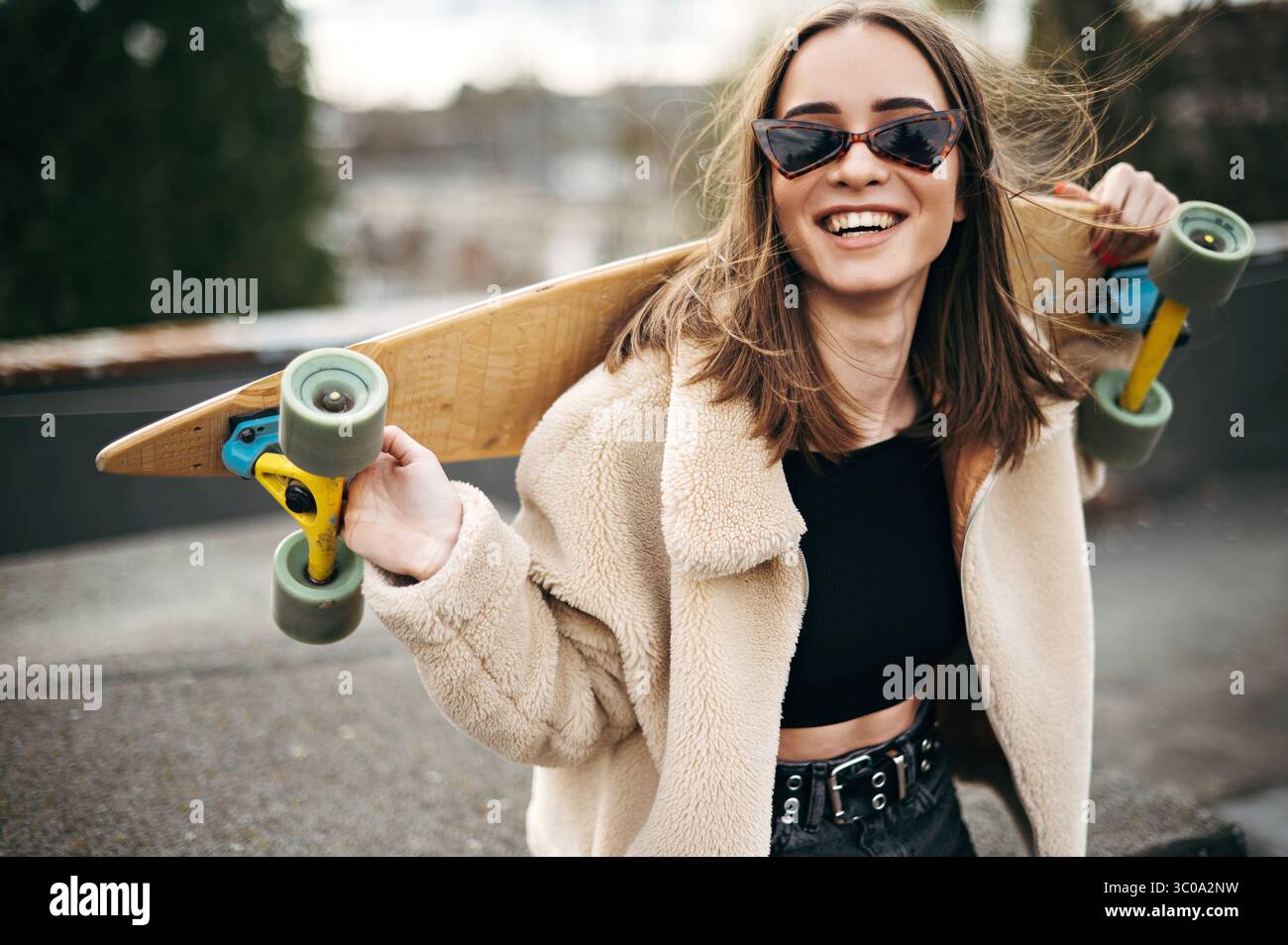 Stilvolle junge Frau, die Skateboard auf den Schultern auf dem Dach hält Stockfoto