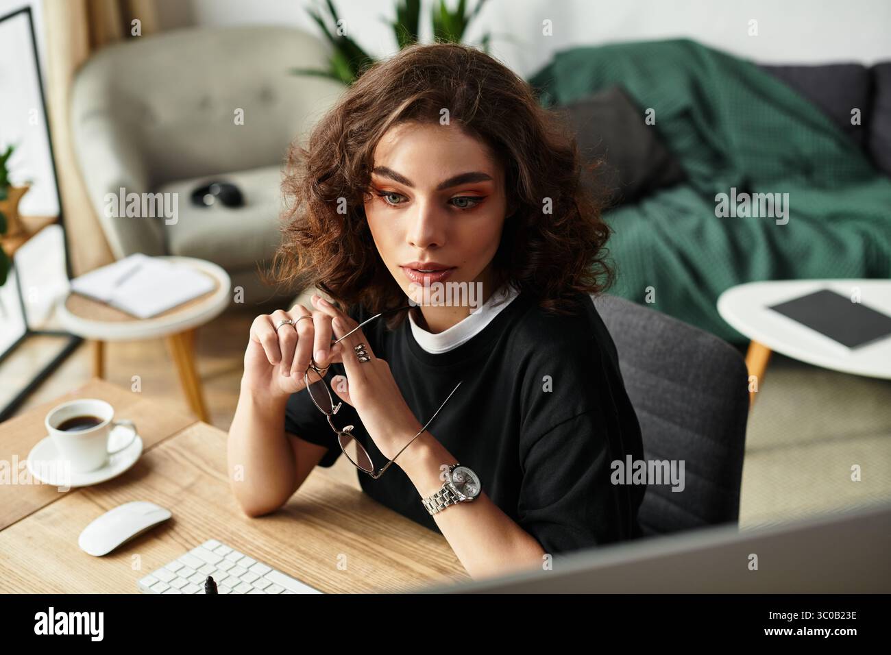 Eine junge Frau mit lockigen Haaren sitzt an ihrem Schreibtisch und beschäftigt sich intensiv mit Fernarbeit von zu Hause aus. Stockfoto