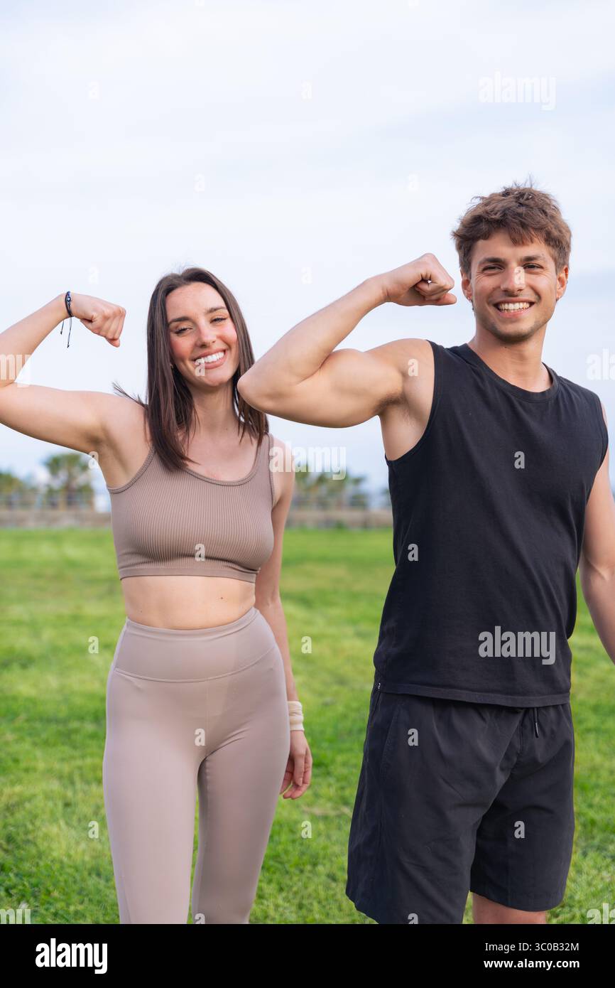 Junges Paar, das Arme biegt und lächelt während des Workouts im Park am Meer Stockfoto