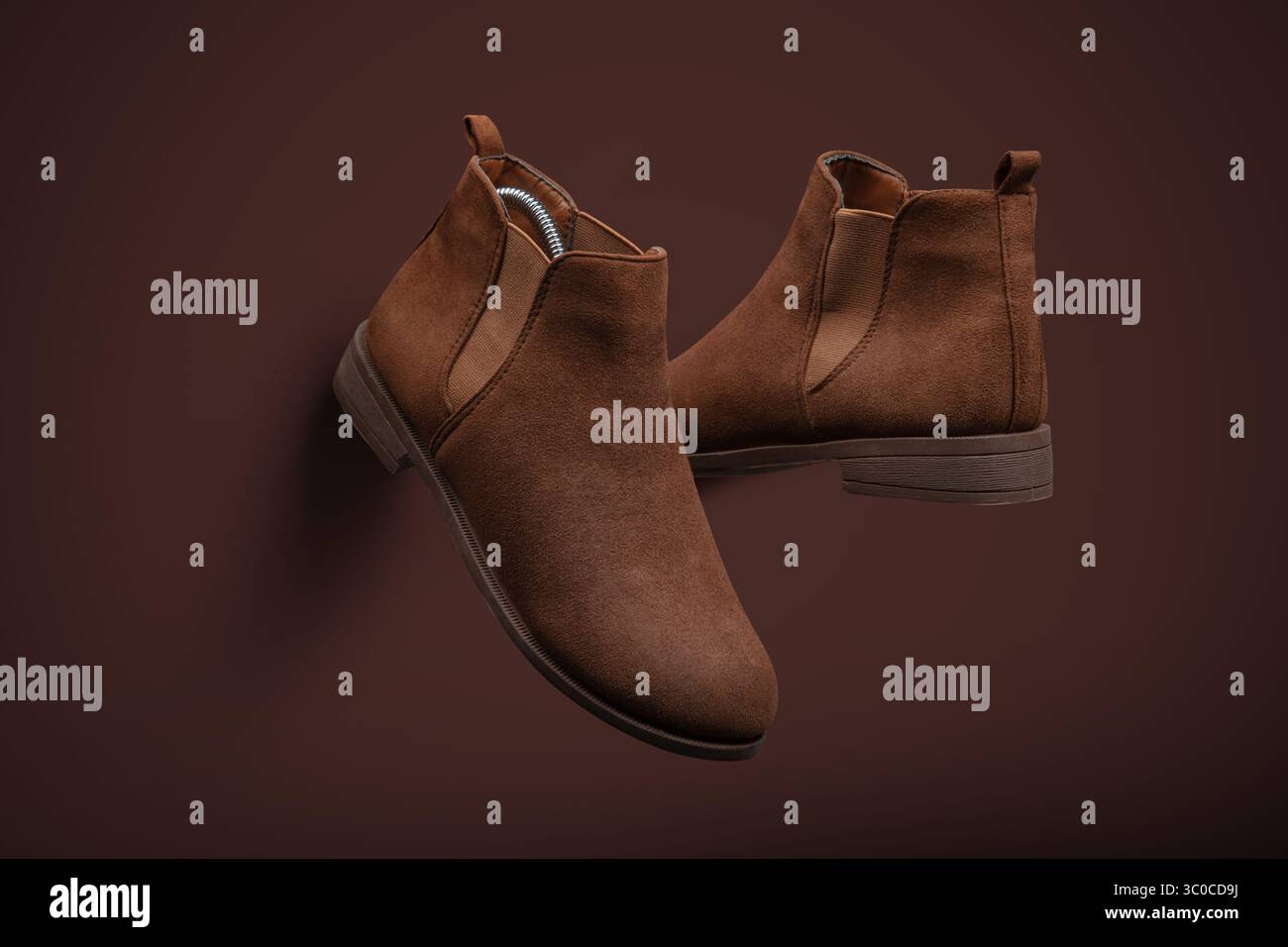 Blick von oben auf ein Paar moderne braune Chelsea-Stiefel aus Wildleder, die diagonal auf einem passenden braunen Hintergrund platziert sind. Minimalistisches Layout und elegante Textur Stockfoto