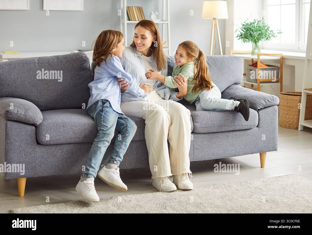 Mutter verbringt Zeit mit ihren Kindern auf der grauen Couch im Wohnzimmer, hat Spaß und lacht zusammen. Stockfoto