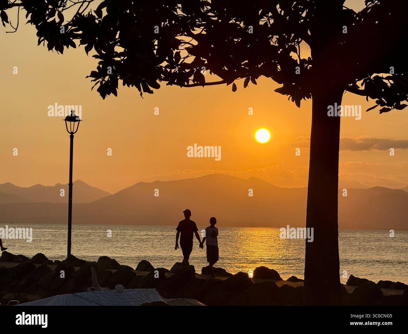 Zwei Personen bei Sonnenuntergang auf dem Steg in Cisano (bei Bardolino) am Gardasee, Italien Stockfoto