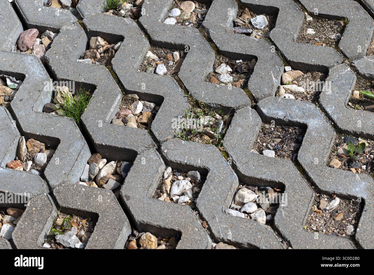 Geometrischer Betonpflaster mit offenen, mit Steinen und sprießendem Grün gefüllten Flächen, die eine Mischung aus organischer und urbaner Ästhetik bieten Stockfoto