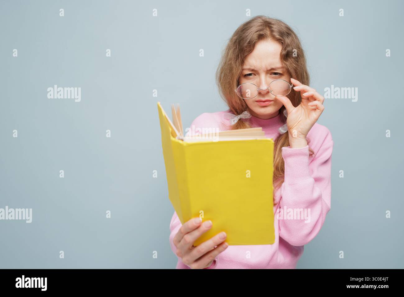 Frau mit Brille, die auf ein Buch schwinzt, Konzept der schlechten Sicht, Schwierigkeiten beim Lesen, Augengesundheit Problem Stockfoto