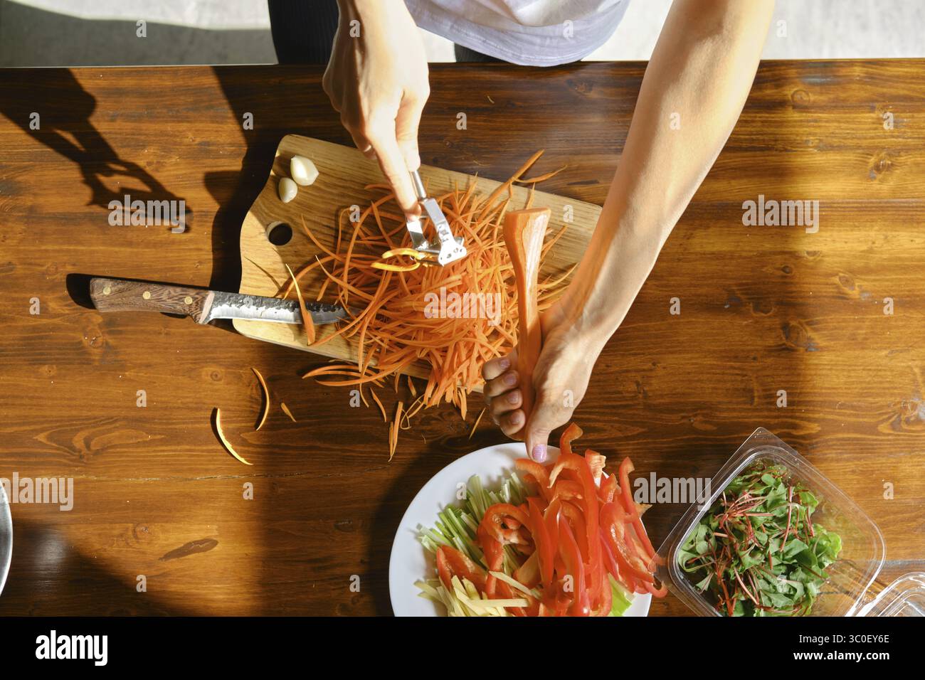 In einer hellen Küche schält und schneidet eine Person mit einem Schnitzermesser Karotten geschickt und in Scheiben Stockfoto