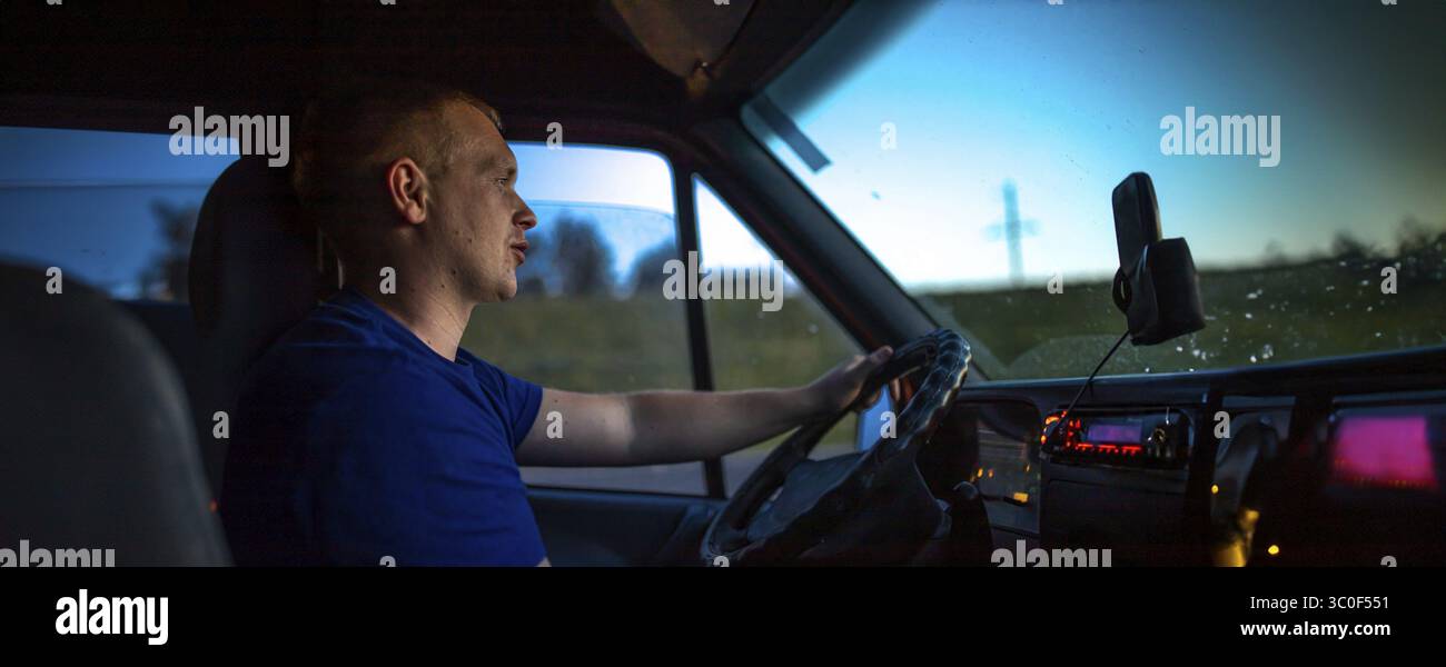 Mann fährt Van in der Dämmerung, fokussierter Look, weiche Innenbeleuchtung Stockfoto