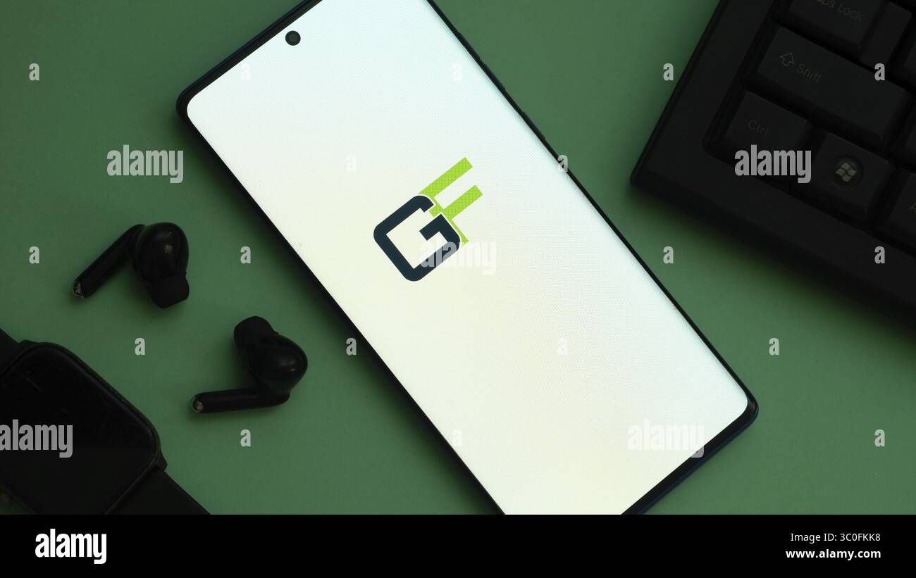Smartphone mit grünem und blauem „GF“-Logo auf grüner Oberfläche mit Zubehör Stockfoto