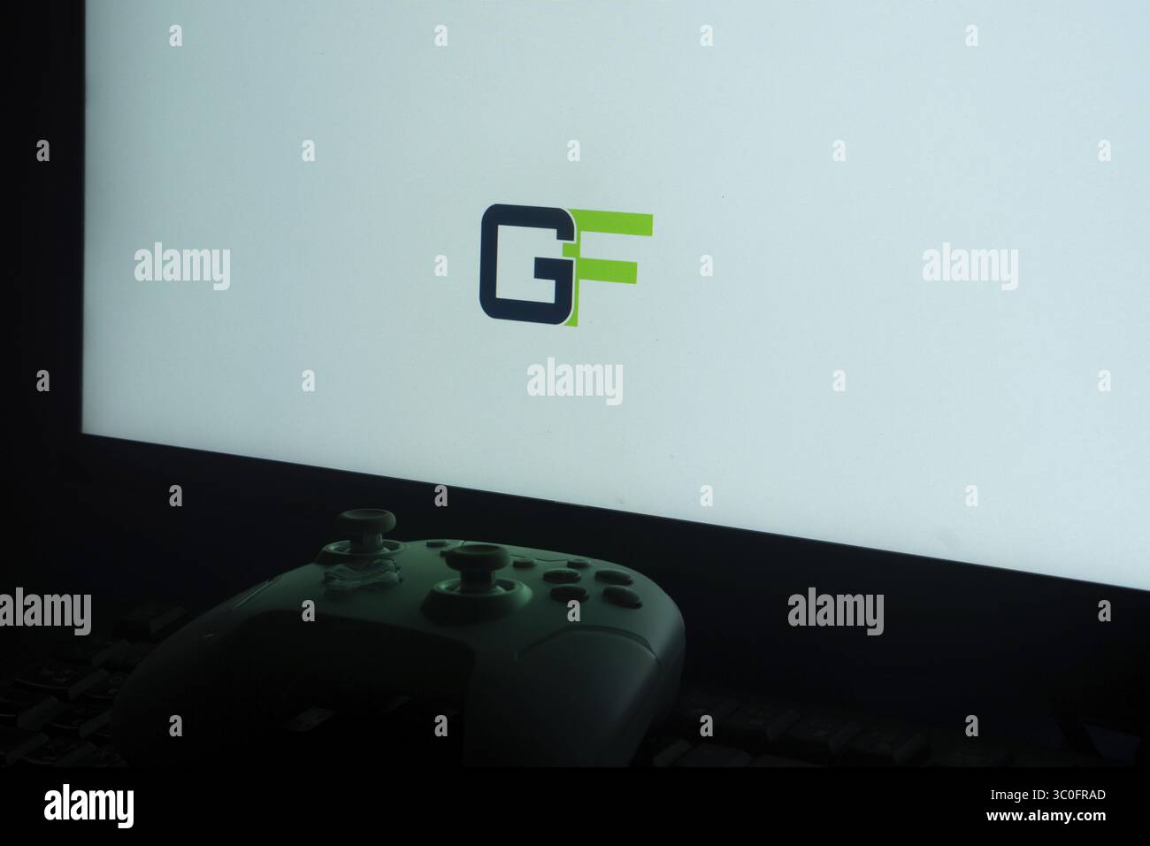 Monitor mit grünem und blauem „GF“-Logo und Gamecontroller im Gaming-Setup Stockfoto
