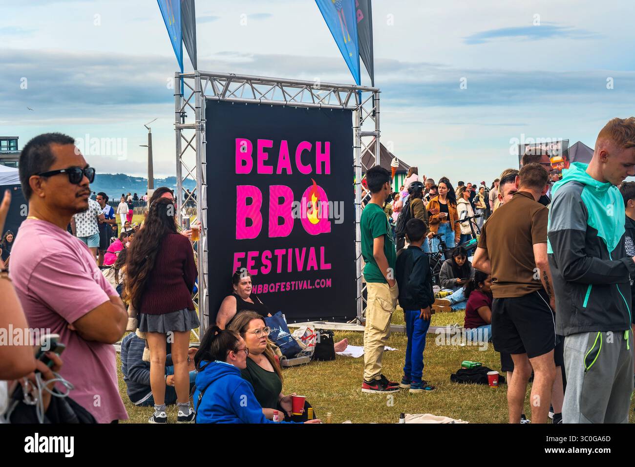 Die Menschenmassen versammeln sich unter dem Schild „BBQ FESTIVAL“ am STRAND in Bray, mit Meerblick und fliegenden Fahnen – 19.07.2025 Stockfoto