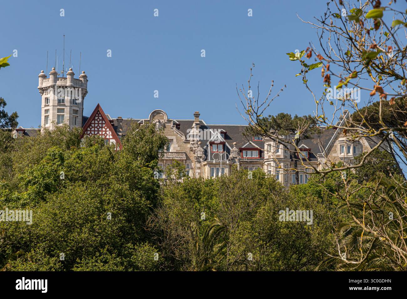 Santander, Spanien. Turm und obere Stockwerke des Palacio de la Magdalena, der sich über einem dichten Walddach erhebt und unter einem klaren Frühlingshimmel auf dem M gefangen gehalten wird Stockfoto