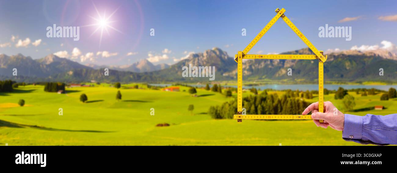 Wohnen auf dem Land, Handschuh in der Natur ein Meterstab ist gefaltet wie ein Haus und wird mit der Hand vor einer unberührte Landschaft, Handschuh in der N Stockfoto