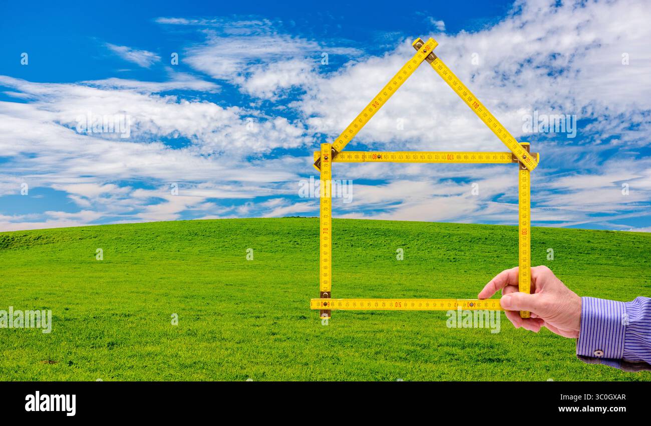 Wohnen auf dem Land, Handschuh in der Natur ein Meterstab ist gefaltet wie ein Haus und wird mit der Hand vor einer unberührte Landschaft, Handschuh in der N Stockfoto