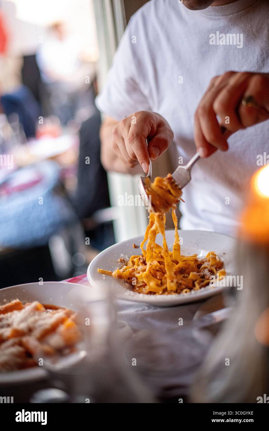 Esskultur, London, Ein junger Mann aus den 20er Jahren, der die Bänder der Tagliatelle auseinander zieht und die Soße mischt und kurz vor dem Essen steht Stockfoto