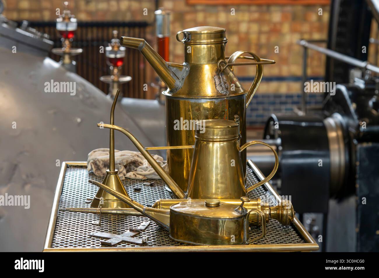 Nahaufnahme von Vintage-Messingölkannen mit nicht fokussierter Dampfmaschine und Vintage-Tropföler im Hintergrund Stockfoto