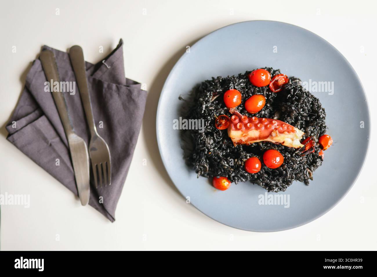 Schwarzes Gourmet-Risotto mit gegrilltem Oktopus und Kirschtomaten auf einem grauen Teller, Feinschmeckergericht aus nächster Nähe. Stockfoto