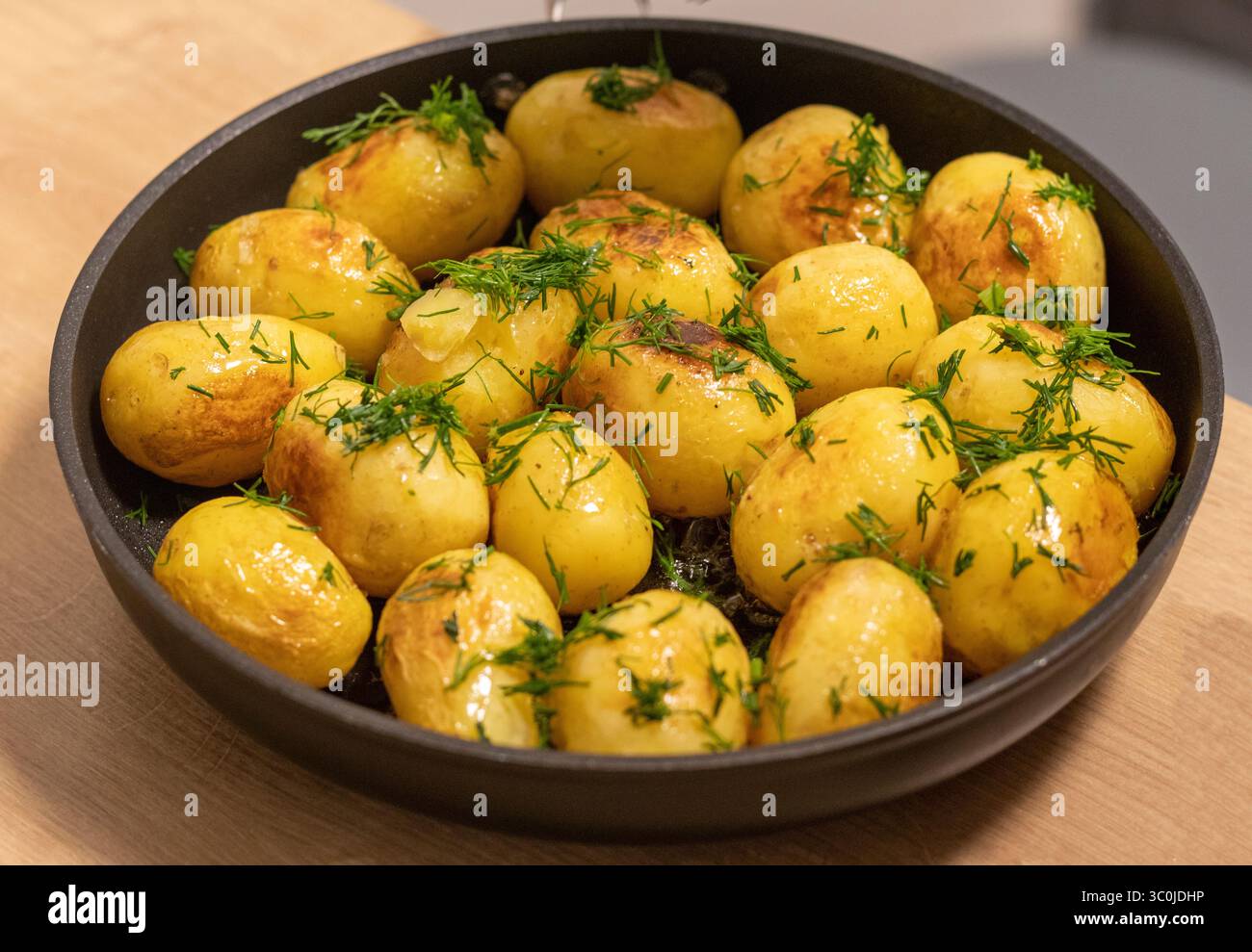 Junge Jackenkartoffeln in einer Pfanne gebraten und mit Kräutern bestreut Stockfoto