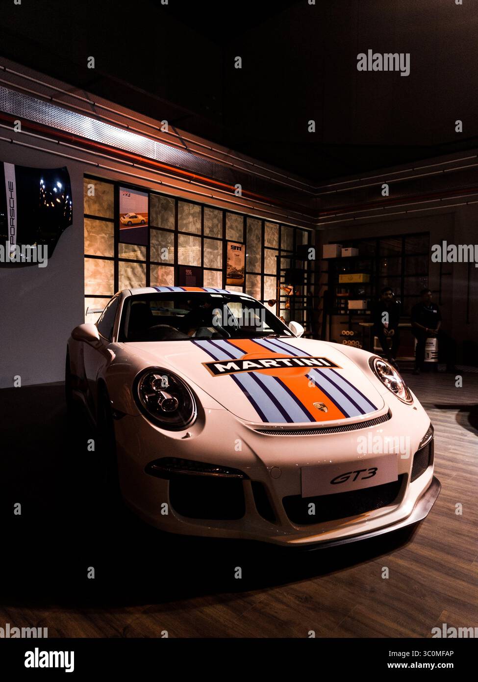 Martini-liverisierter Porsche 911 GT3 Sportwagen, der in einem luxuriösen Ausstellungsraum geparkt wird, mit dezenter Umgebungsbeleuchtung, die schlankes Design und Performance-Ästhetik betont Stockfoto