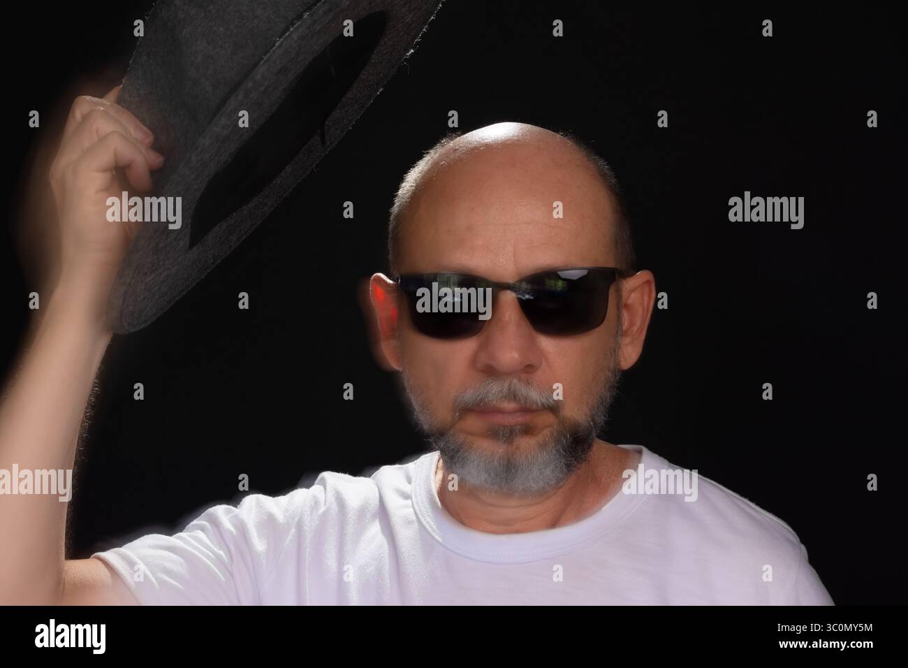 Künstlerisches Porträt eines bärtigen Glatzen-Mannes in weißem Hemd, der Bewegungen mit Armen und Händen verwischt. Schwarzer Hintergrund. Stockfoto