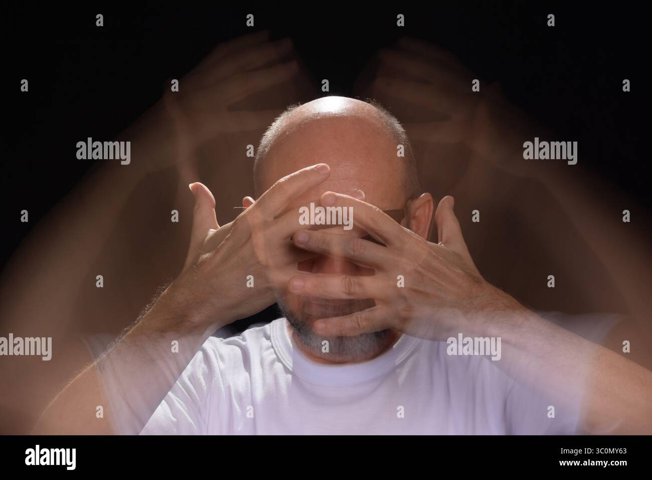 Künstlerisches Porträt eines bärtigen Glatzen-Mannes in weißem Hemd, der Bewegungen mit Armen und Händen verwischt. Schwarzer Hintergrund. Stockfoto