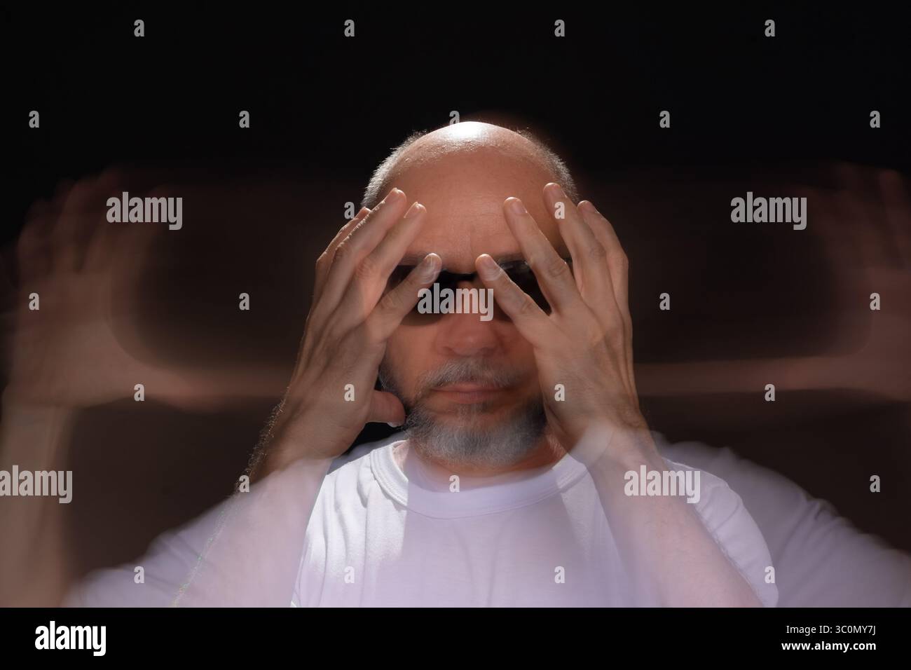 Künstlerisches Porträt eines bärtigen Glatzen-Mannes in weißem Hemd, der Bewegungen mit Armen und Händen verwischt. Schwarzer Hintergrund. Stockfoto