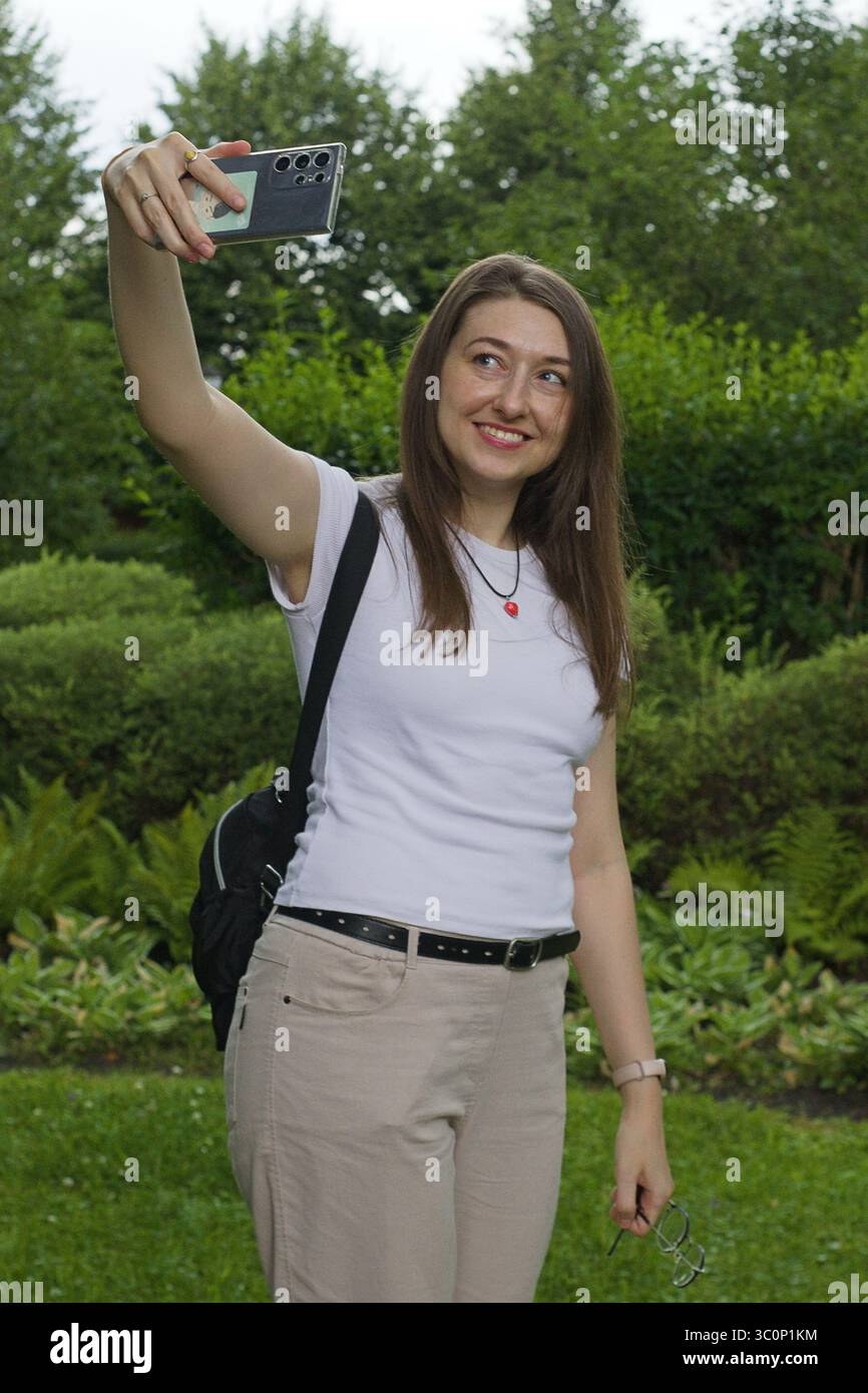 Touristikerin macht ein Selfie in einem grünen Park, hält ihr Smartphone und genießt dabei ihren Reisemoment. Lässige Naturszene, die moderne Tour widerspiegelt Stockfoto