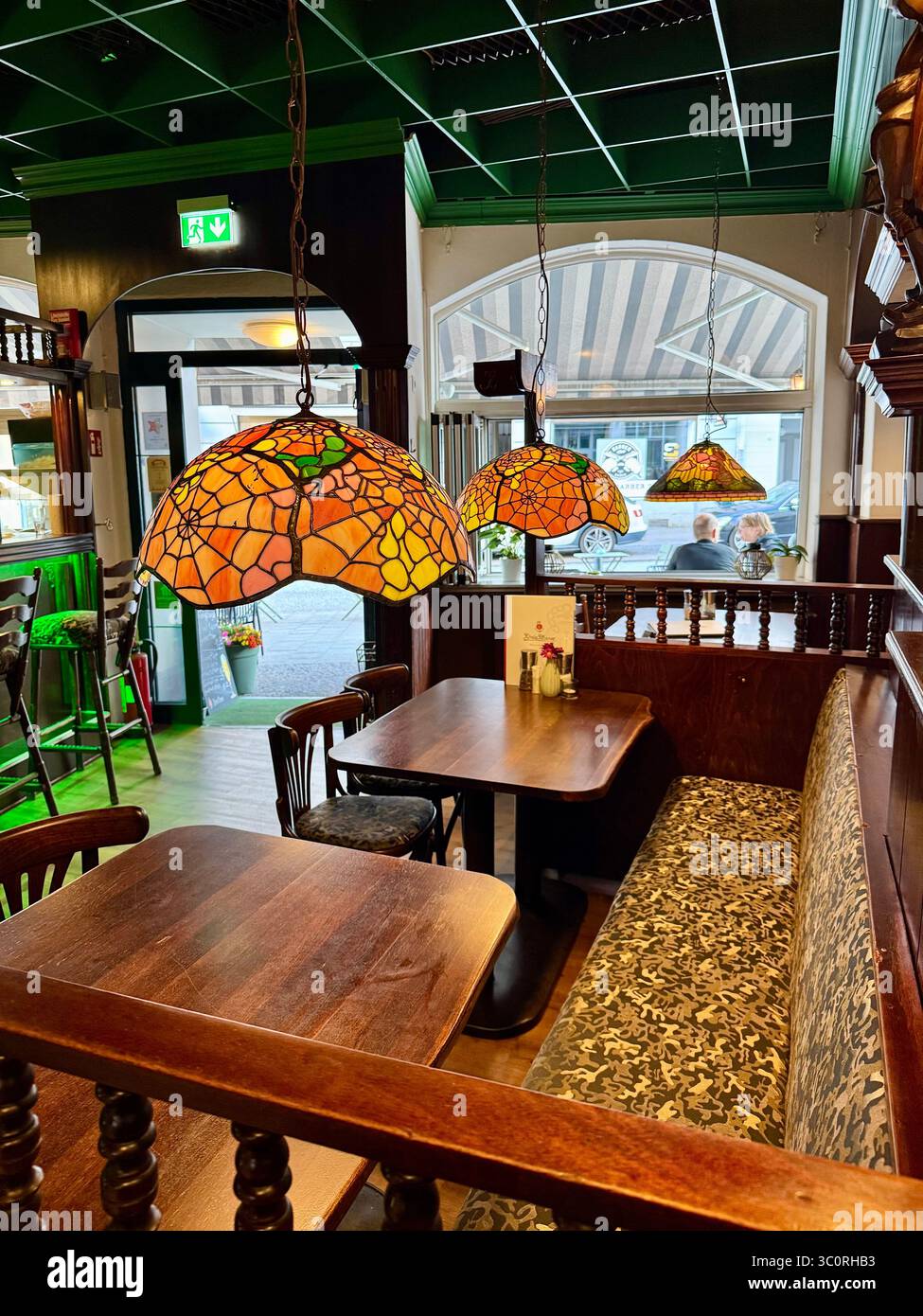 Gemütliches Interieur eines traditionellen Restaurants in Lübeck, Deutschland, mit warmer Beleuchtung mit Buntglas-Pendelleuchten, Holzmöbeln und Blick auf - Smartphone-aufgenommenes Stockfoto